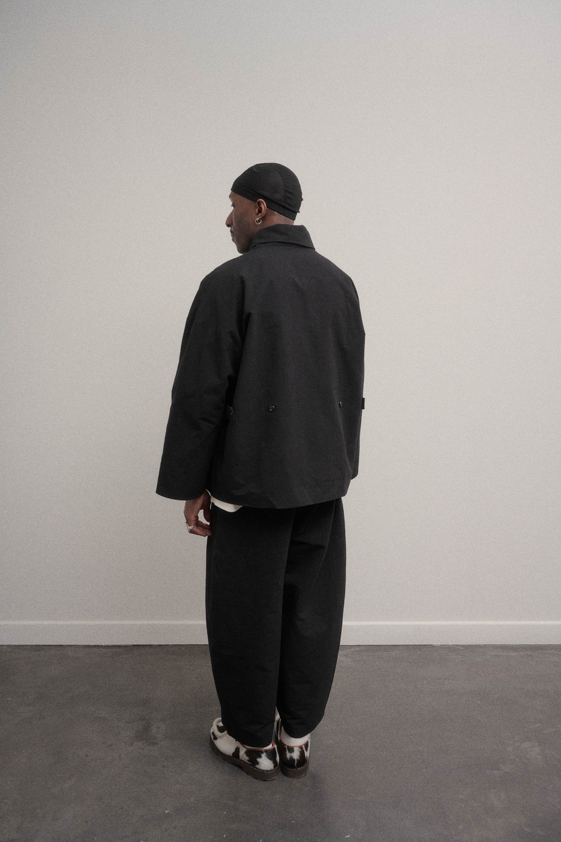 Veste oversize à col arrondi de la marque Aïdama en mélange de coton et papier japonais noir. Portée ouverte par un mannequin homme et vu de dos.