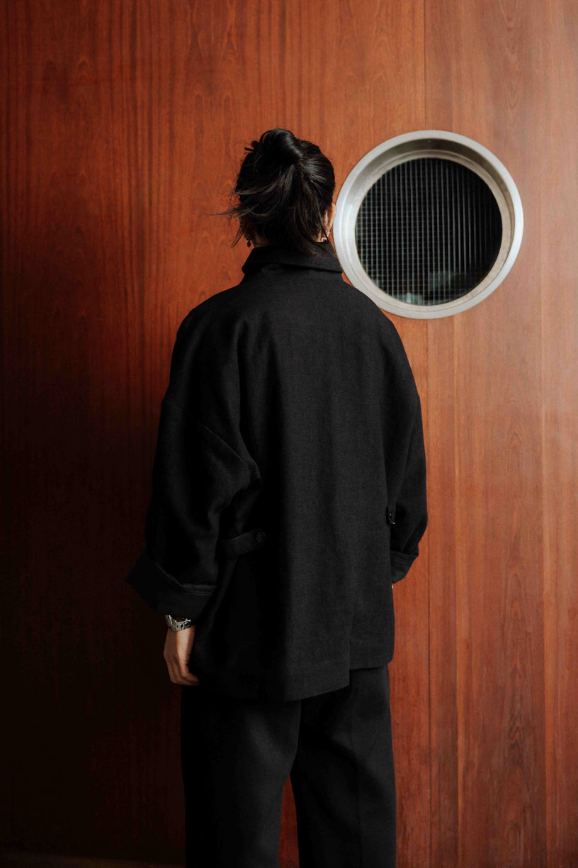 Veste oversize à col arrondi de la marque Aïdama, modèle Gunbai en laine et lin noir Portée fermée par un mannequin homme et vue de dos.