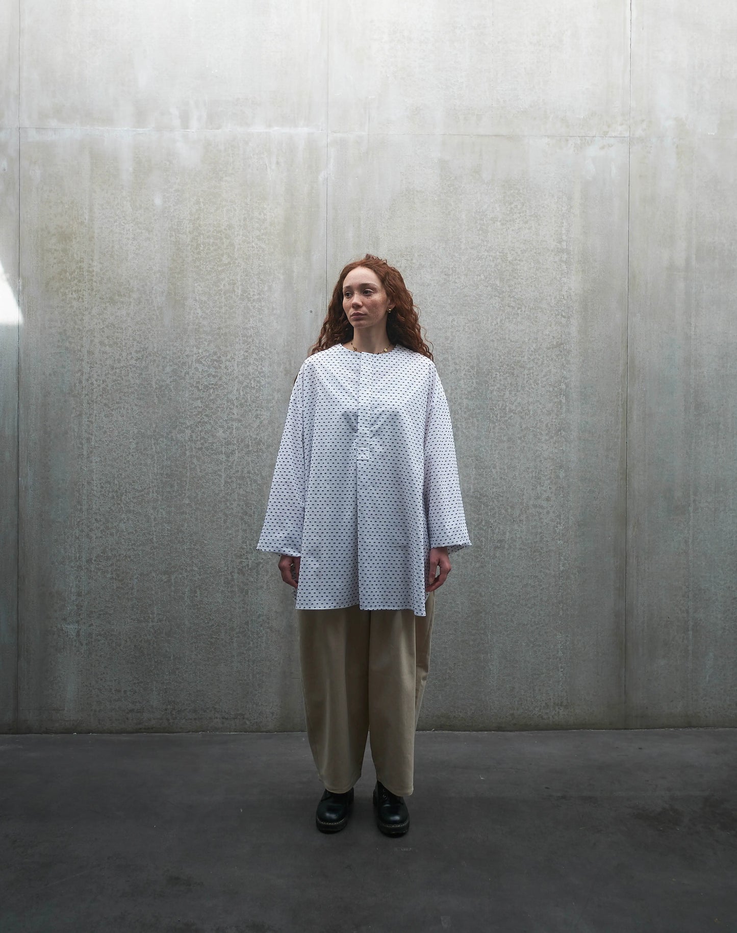 Chemise oversize à manches longues et col rond Aïdama modèle Ao en coton blanc à pois bleus. Portée par une mannequin femme et vue de face.