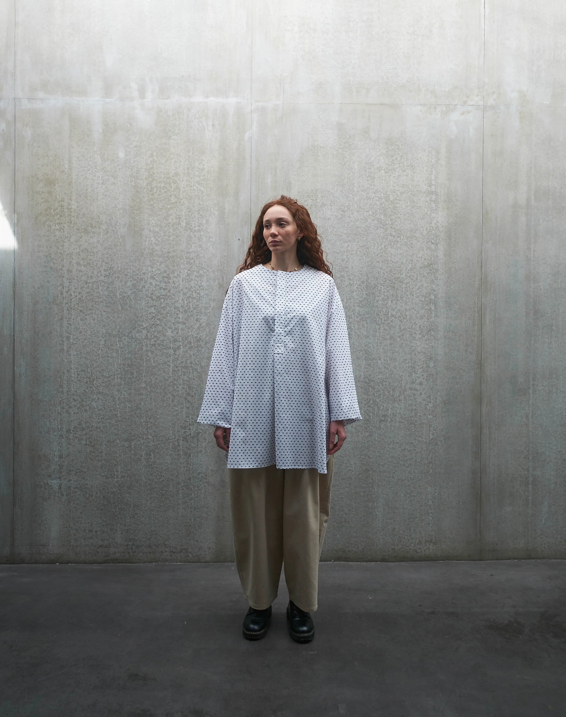 Chemise oversize à manches longues et col rond Aïdama modèle Ao en coton blanc à pois bleus. Portée par une mannequin femme et vue de face.