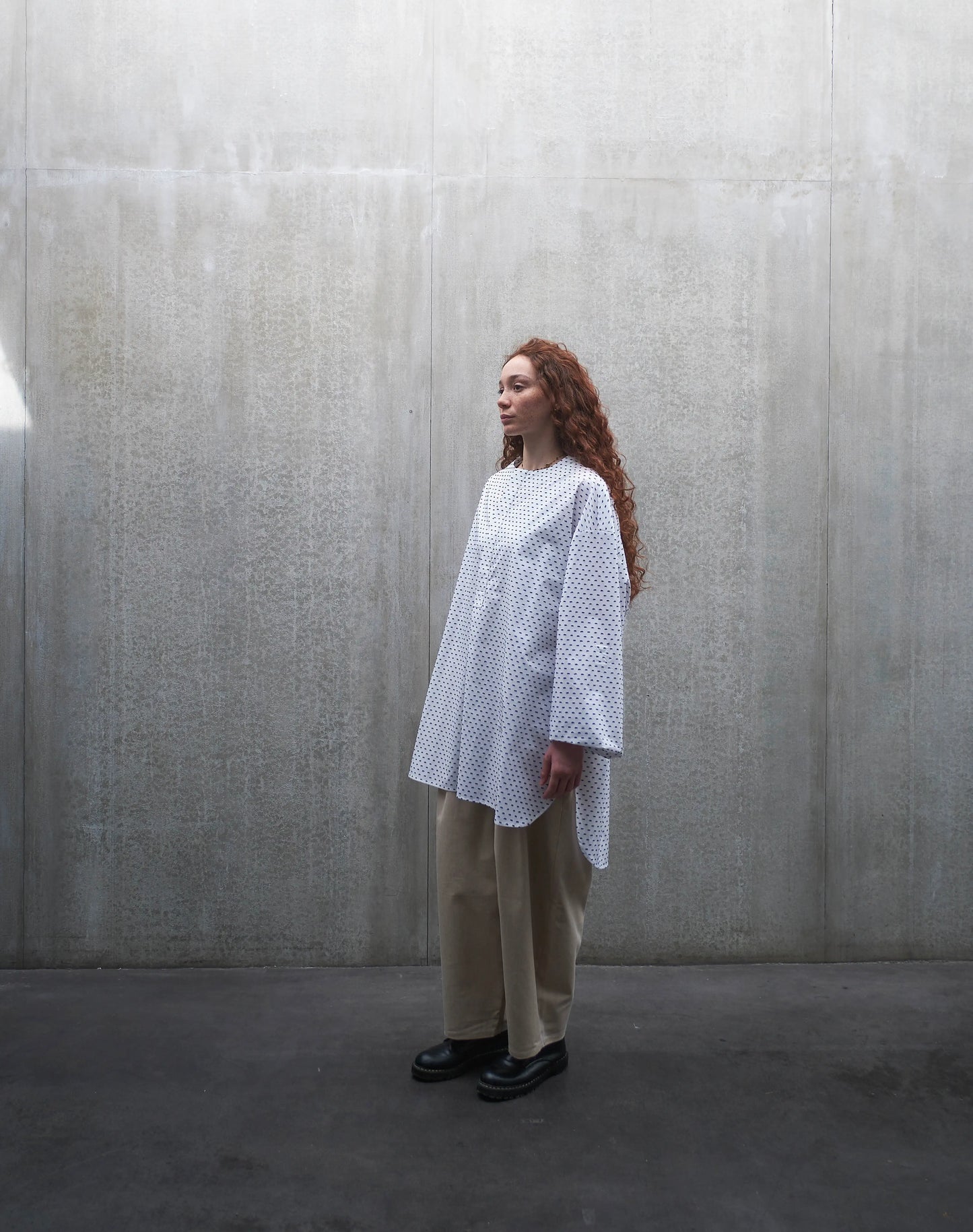 Chemise oversize à manches longues et col rond Aïdama modèle Ao en coton blanc à pois bleus. Portée par une mannequin femme et vue de profil.