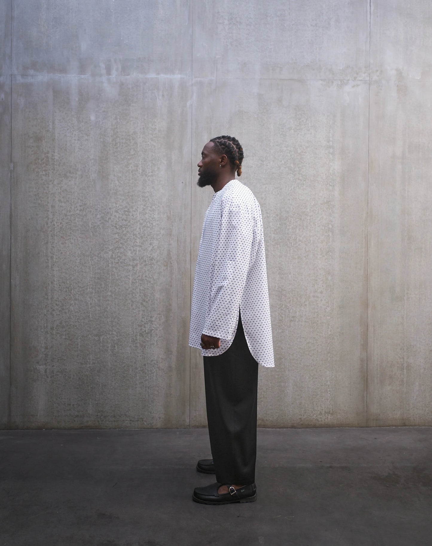 Chemise oversize à manches longues et col rond Aïdama modèle Ao en coton blanc à pois bleus. Portée par un mannequin homme et vue de profil.