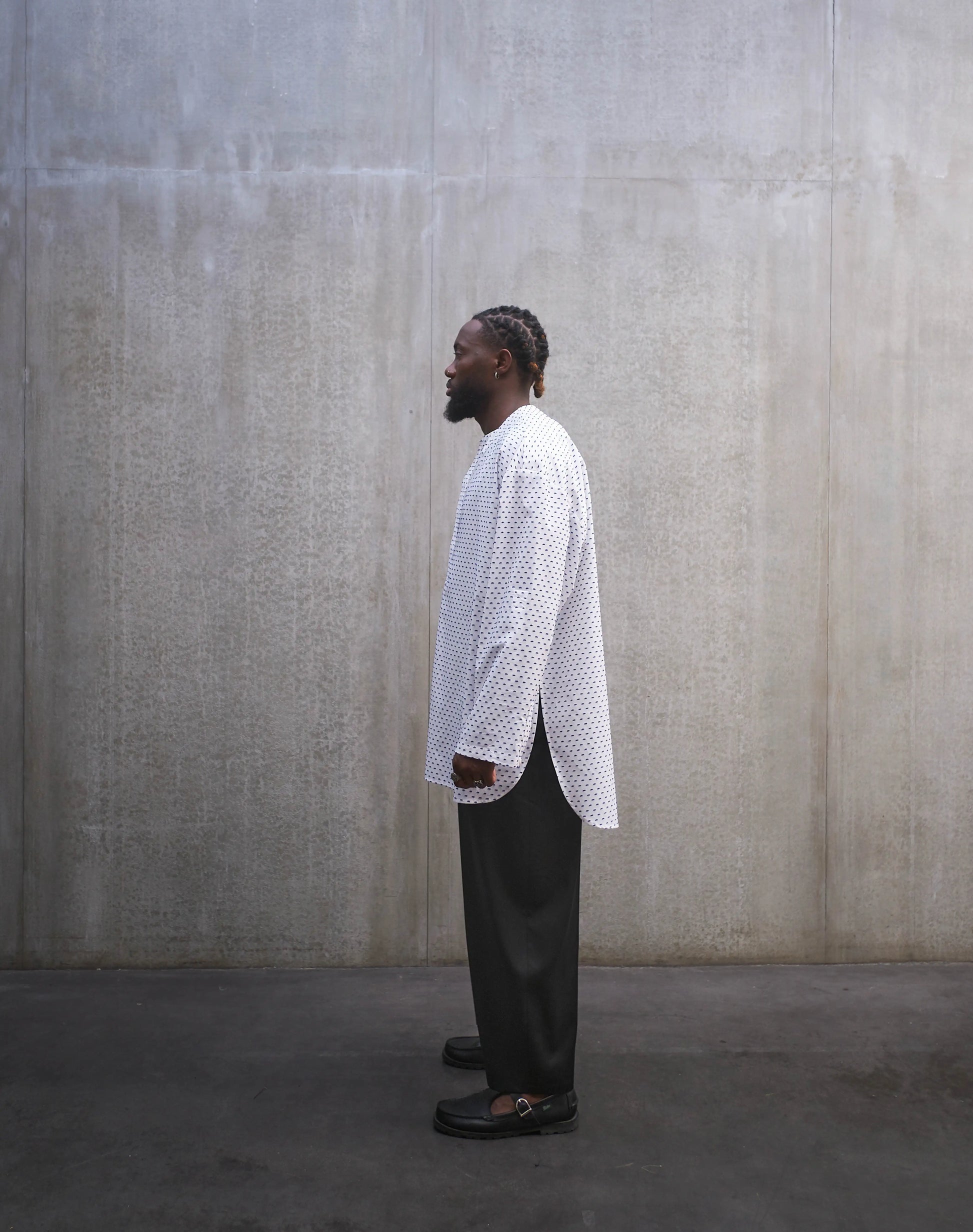 Chemise oversize à manches longues et col rond Aïdama modèle Ao en coton blanc à pois bleus. Portée par un mannequin homme et vue de profil.