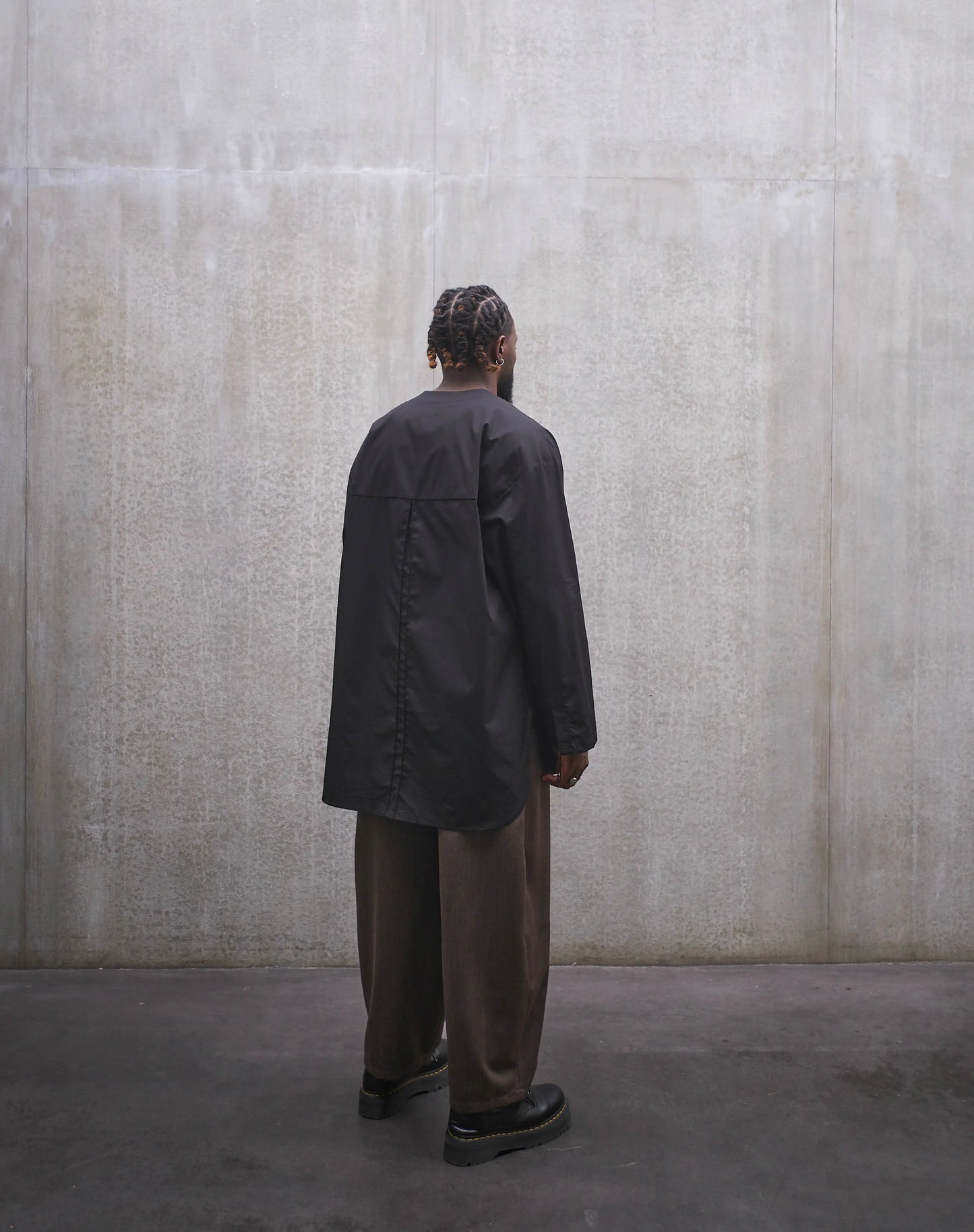 Chemise oversize à manche longue et col rond Aïdama modèle Ao en popeline de coton noir. Portée par un mannequin homme et vue de dos.