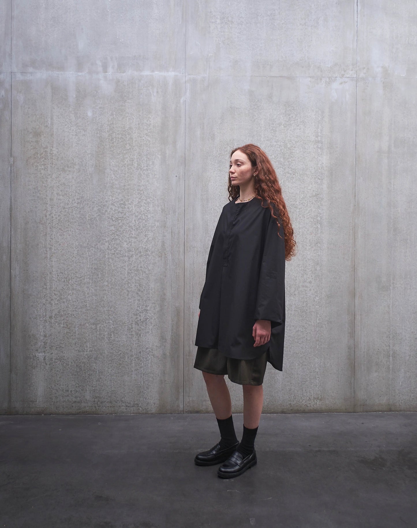 Chemise oversize à manche longue et col rond Aïdama modèle Ao en popeline de coton noir. Portée par une mannequin femme et vue de profil.