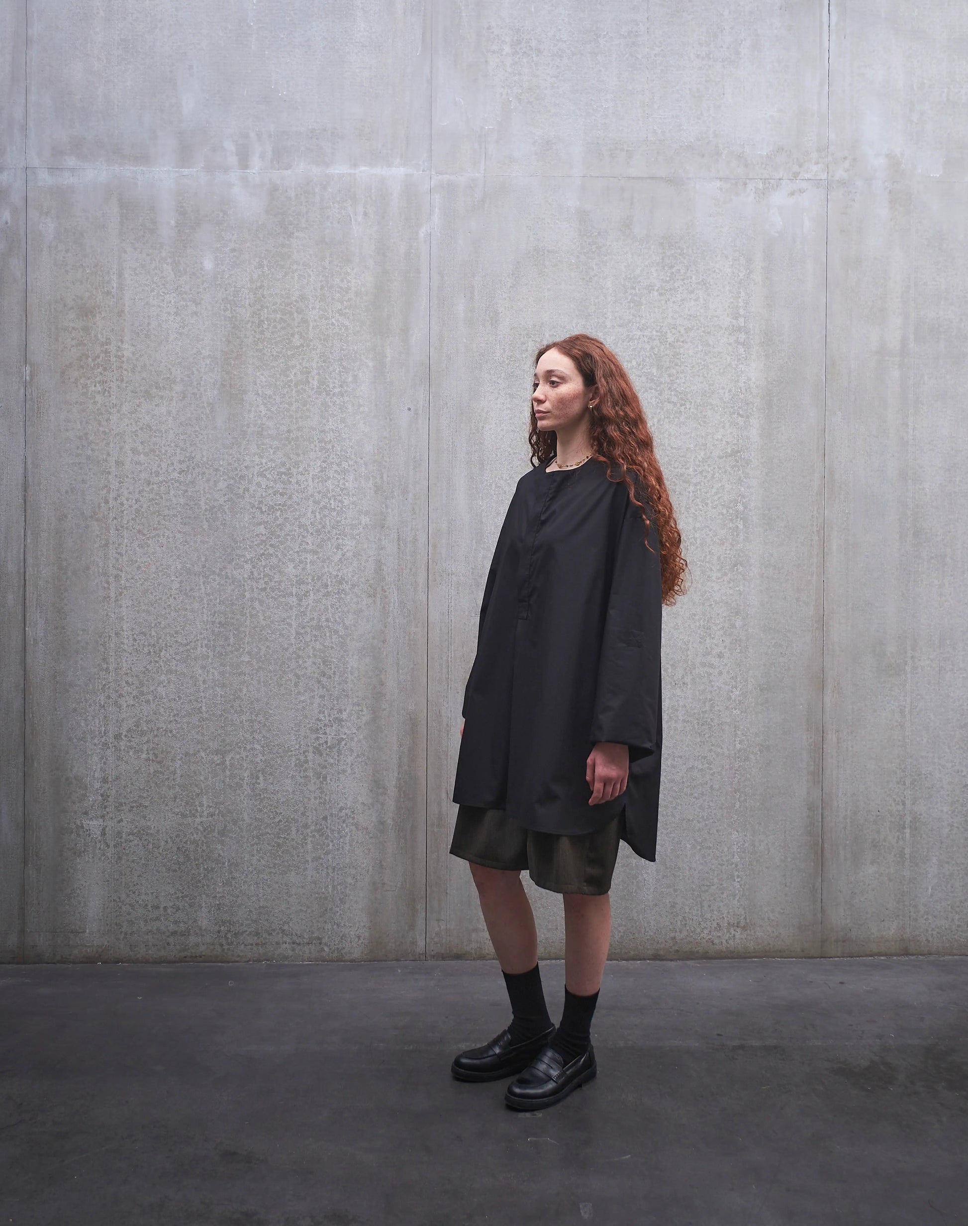 Chemise oversize à manche longue et col rond Aïdama modèle Ao en popeline de coton noir. Portée par une mannequin femme et vue de profil.