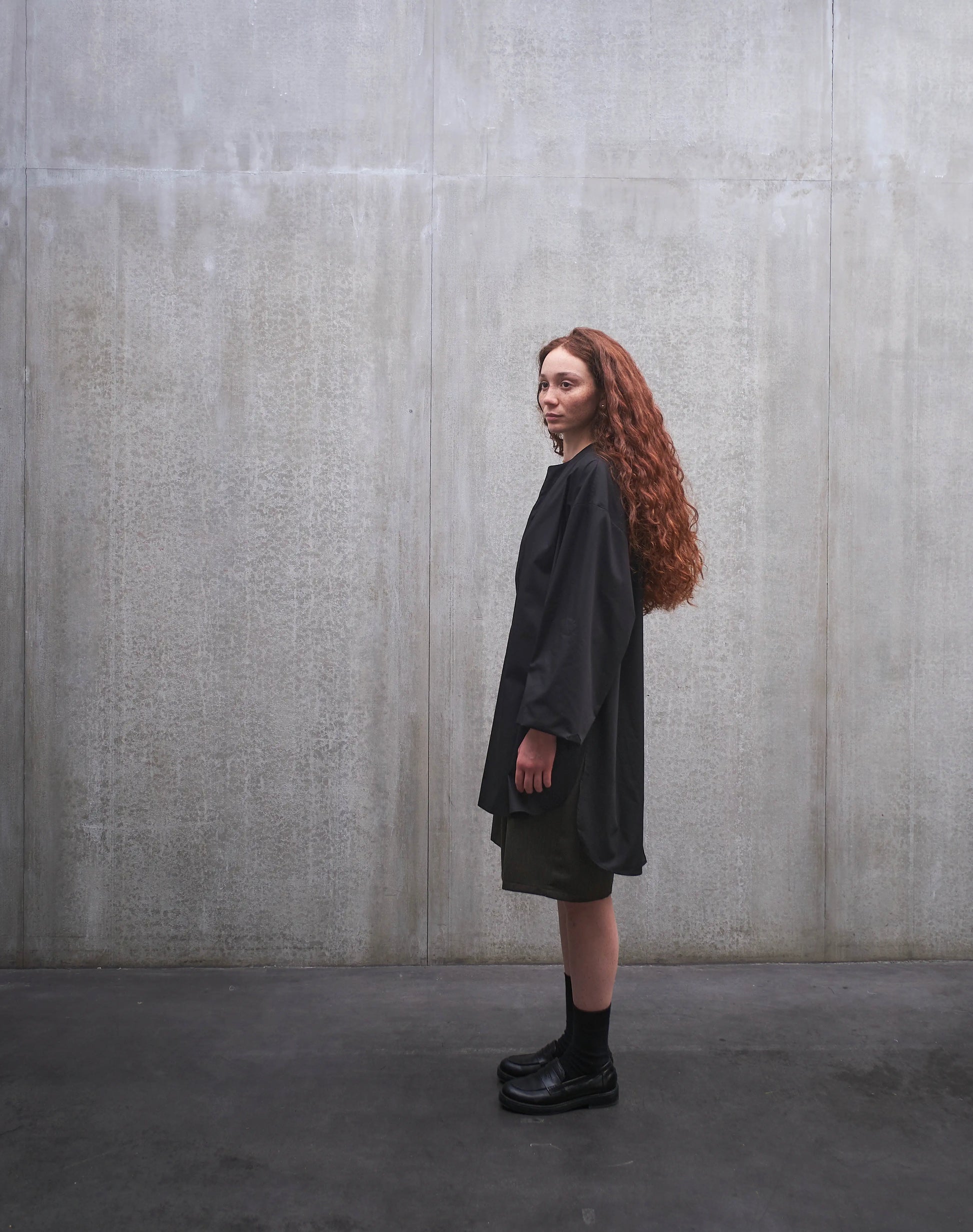 Chemise oversize à manche longue et col rond Aïdama modèle Ao en popeline de coton noir. Portée par une mannequin femme et vue de profil.