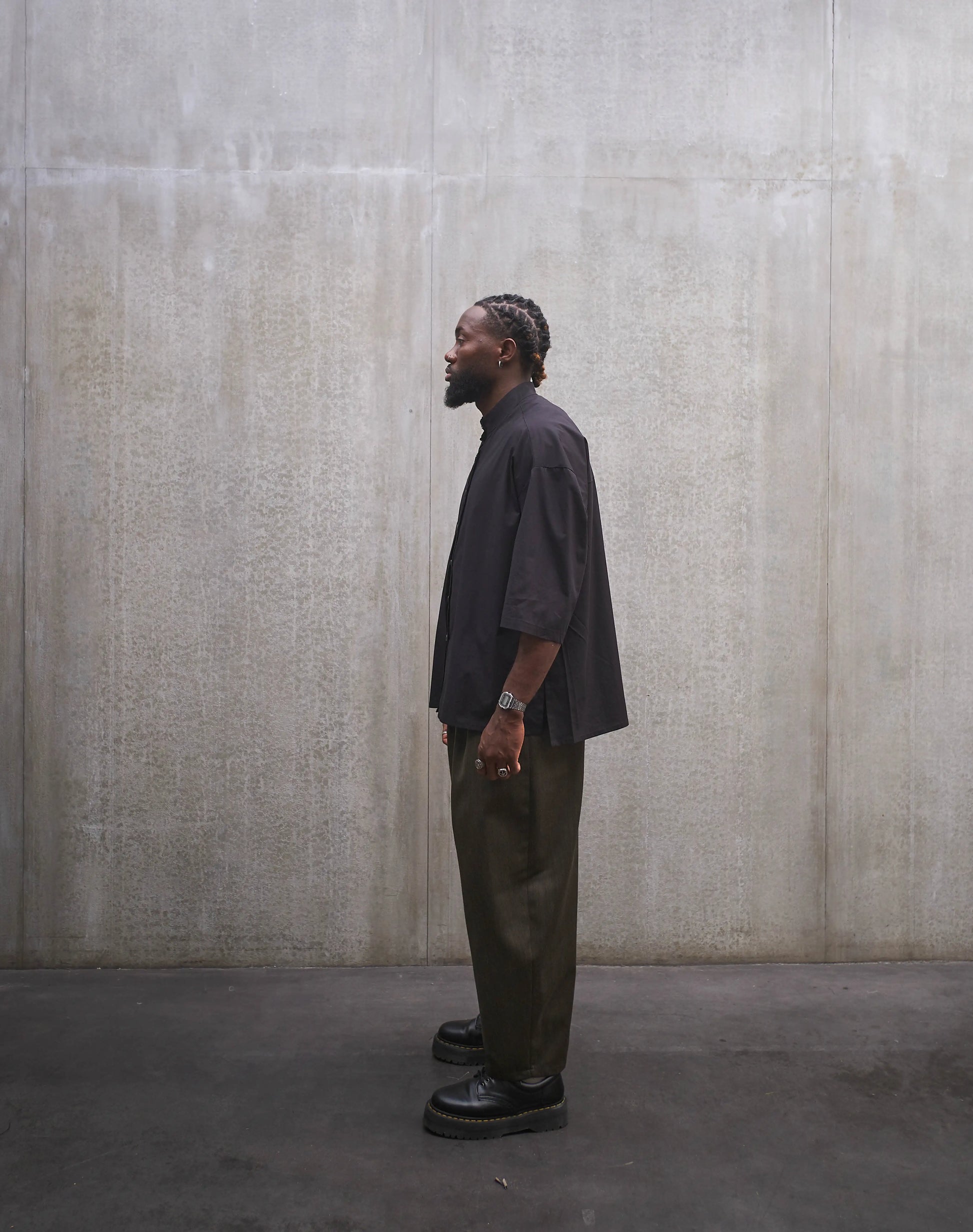 Chemise oversize à col officier de la marque Aïdama, modèle Kita, coupe boxy en popeline de coton noire. Portée par un mannequin homme et vue de profil.