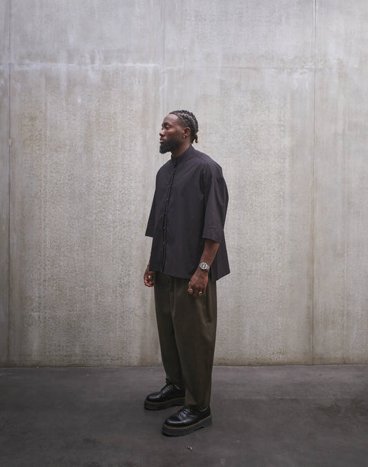 Chemise oversize à col officier de la marque Aïdama, modèle Kita, coupe boxy en popeline de coton noire. Portée par un mannequin homme et vue de trois quarts.