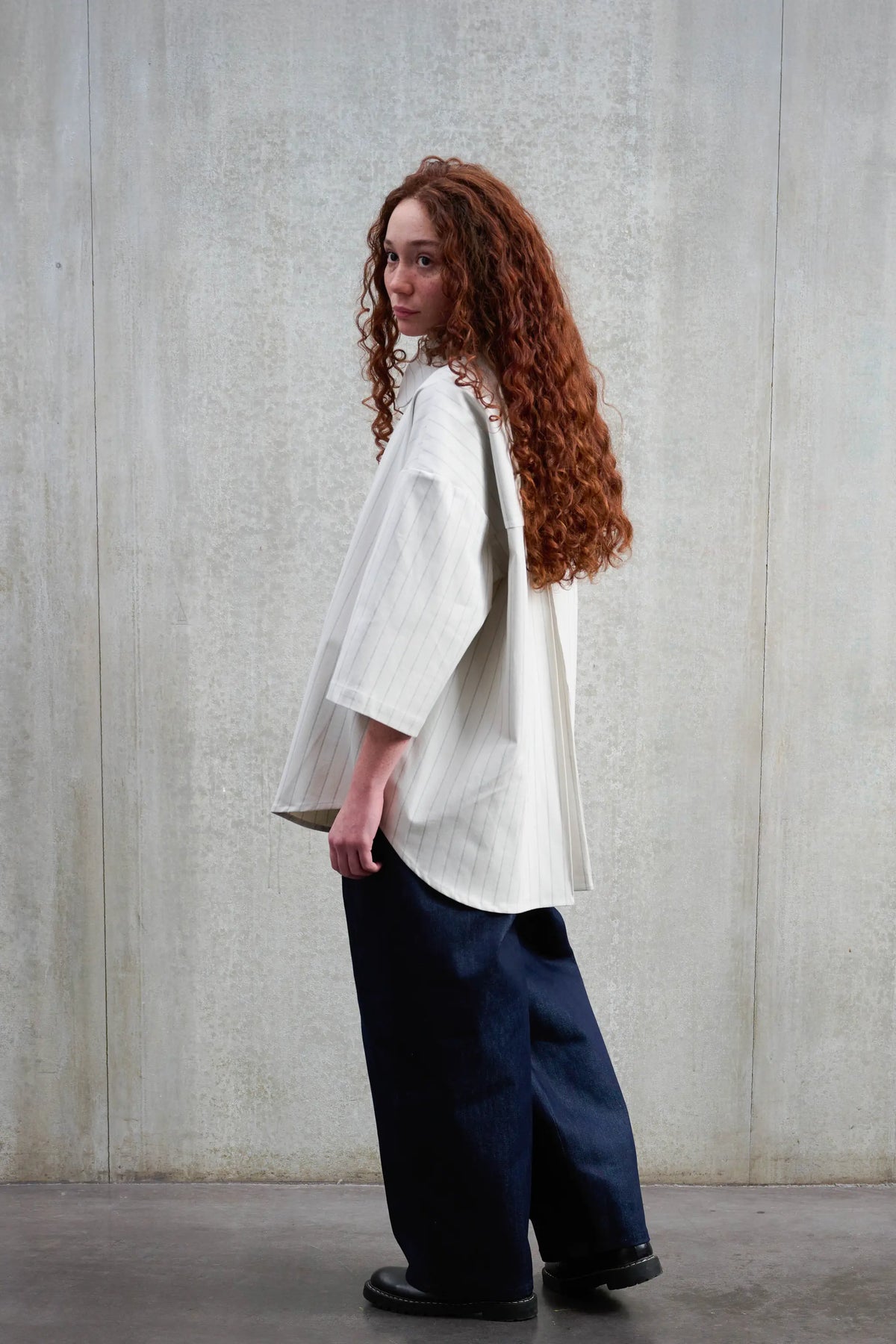 Chemise arrondie oversize de la marque Aïdama, modèle Marui en coton blanc à rayures tennis. Portée par une femme et vue de dos.
