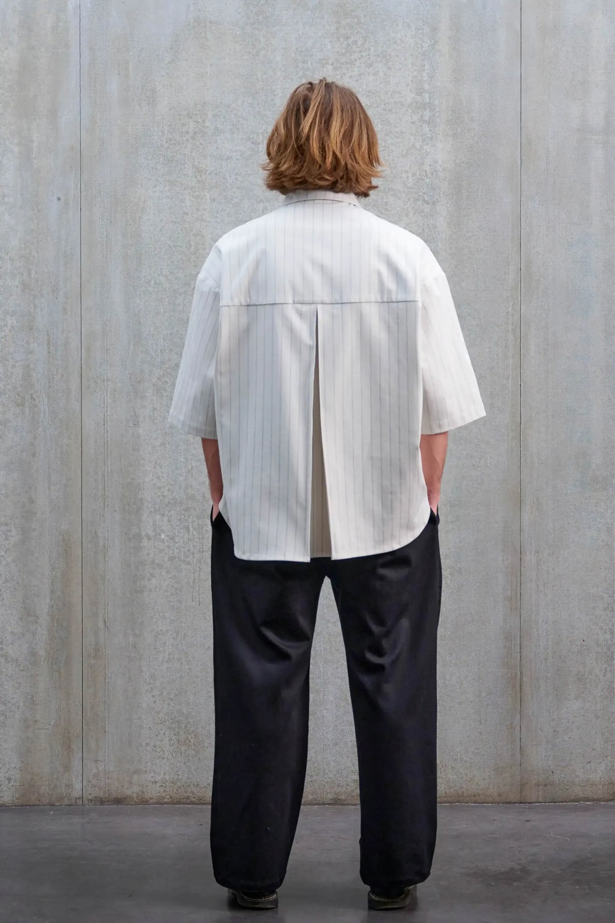 Chemise arrondie oversize de la marque Aïdama, modèle Marui en coton blanc à rayures tennis. Portée par une femme et vue de dos.