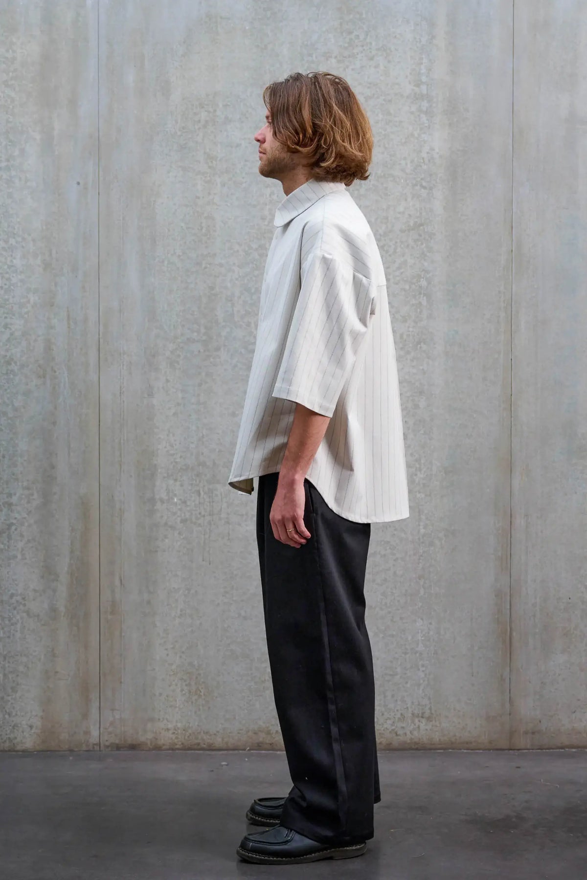 Chemise arrondie oversize de la marque Aïdama, modèle Marui en coton blanc à rayures tennis. Portée par un mannequin homme et vue de profil.