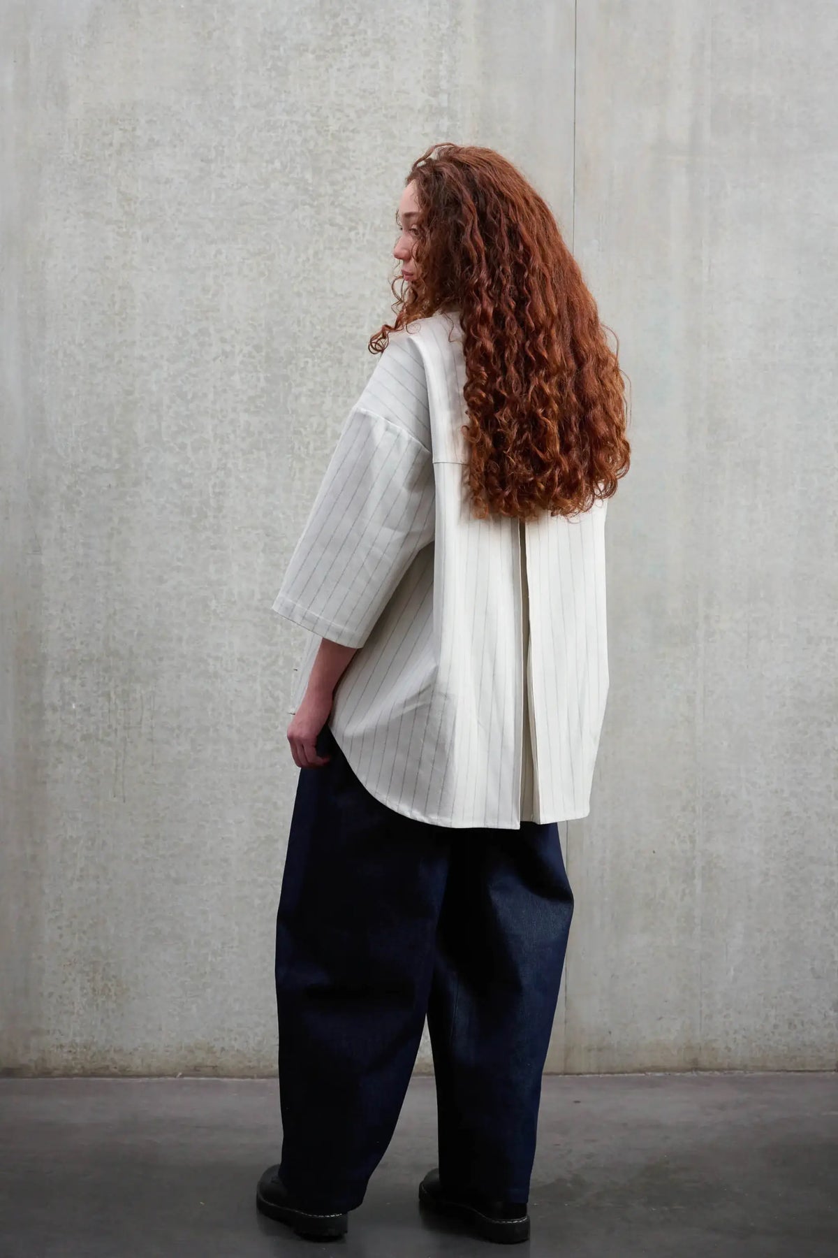 Chemise arrondie oversize de la marque Aïdama, modèle Marui en coton blanc à rayures tennis. Portée par une femme et vue de dos.