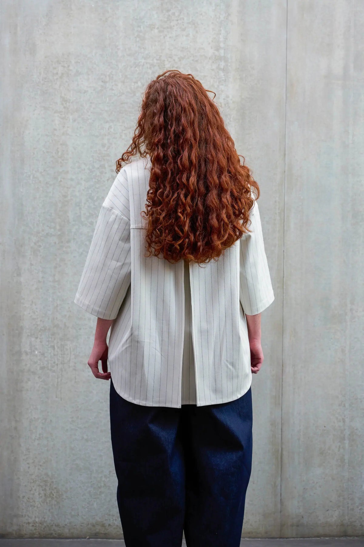 Chemise arrondie oversize de la marque Aïdama, modèle Marui en coton blanc à rayures tennis. Portée par une femme et vue de dos.