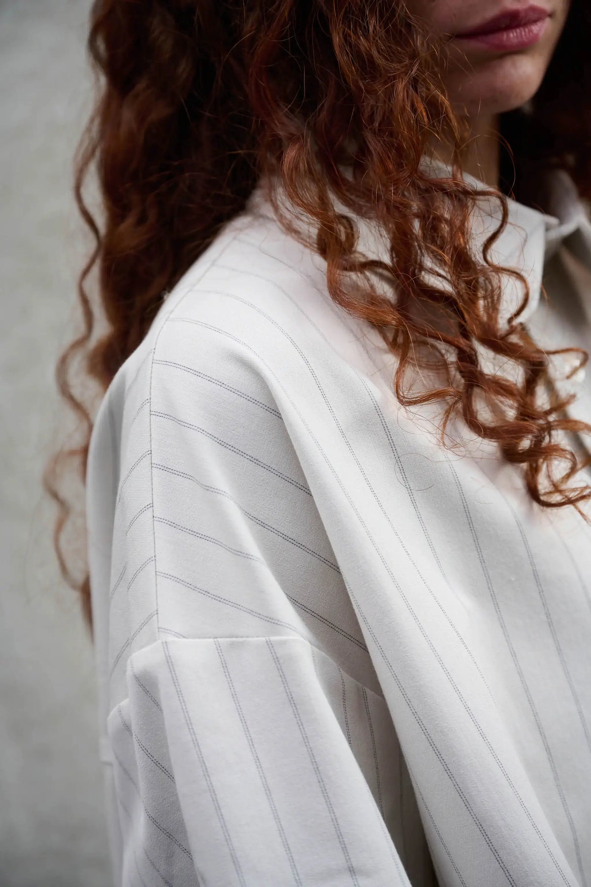 Chemise arrondie oversize de la marque Aïdama, modèle Marui en coton blanc à rayures tennis. Portée par une femme et vue zoomée sur l'épaule.
