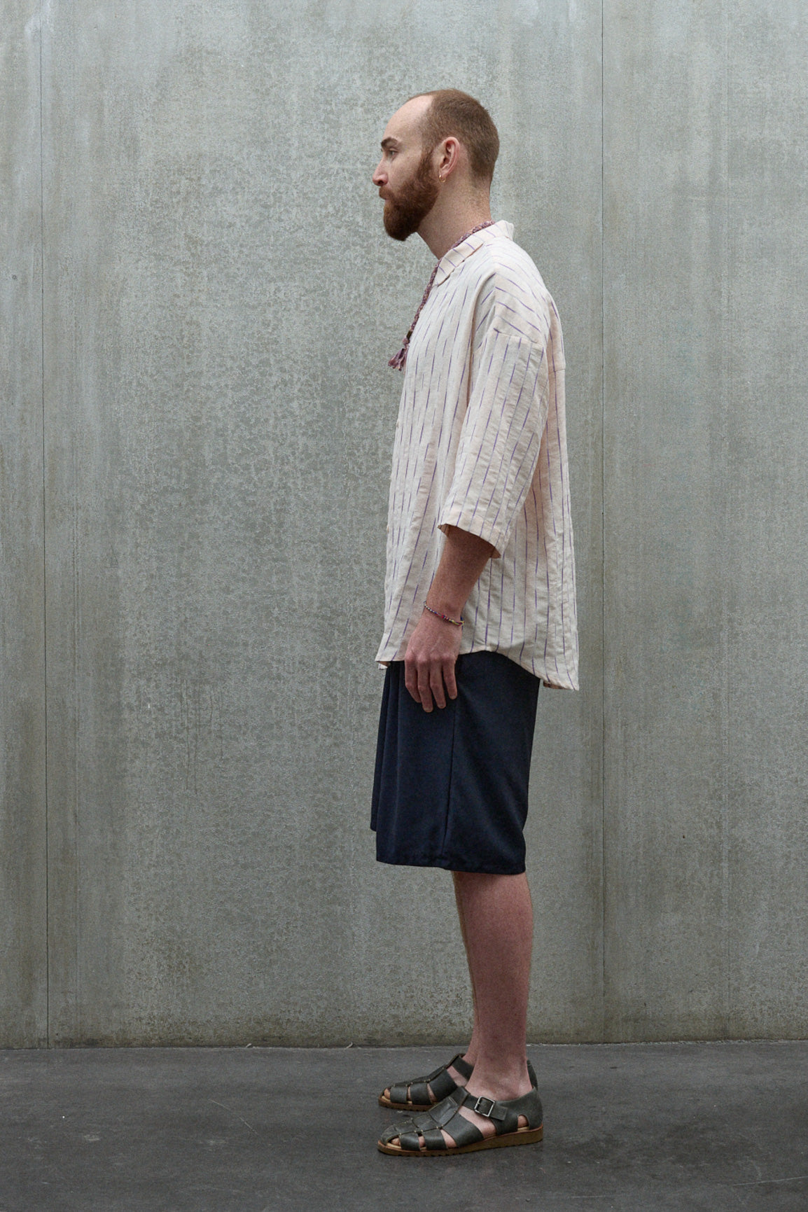 Chemise oversize à manches courtes et col club de la marque Aïdama, modèle Marui en coton rose à rayures violettes. Portée par un mannequin homme et vue de profil.