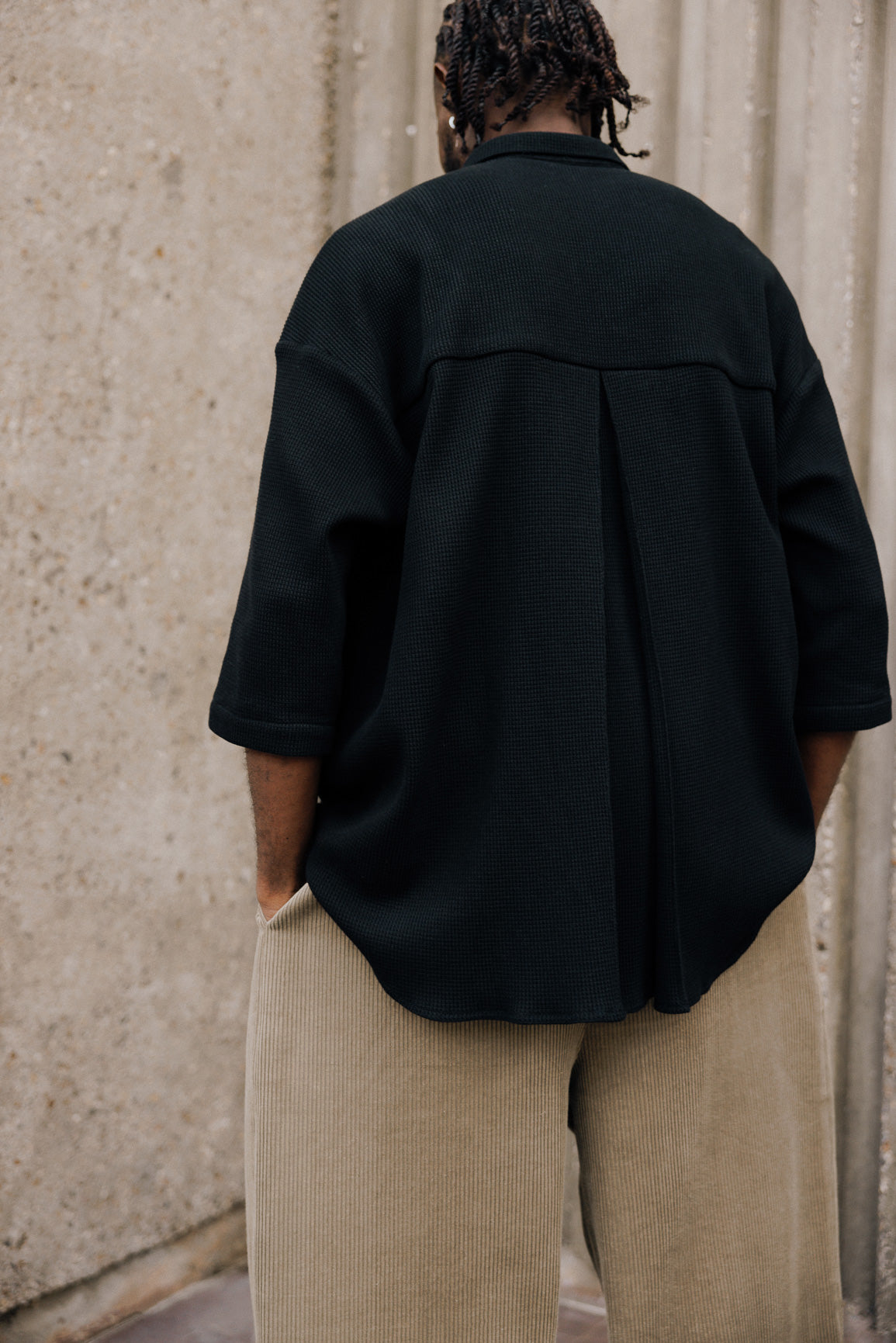Chemise oversize à manches courtes et col club de la marque Aïdama, modèle Marui en coton nid d’abeille noir. Portée par un mannequin homme et vue de dos.