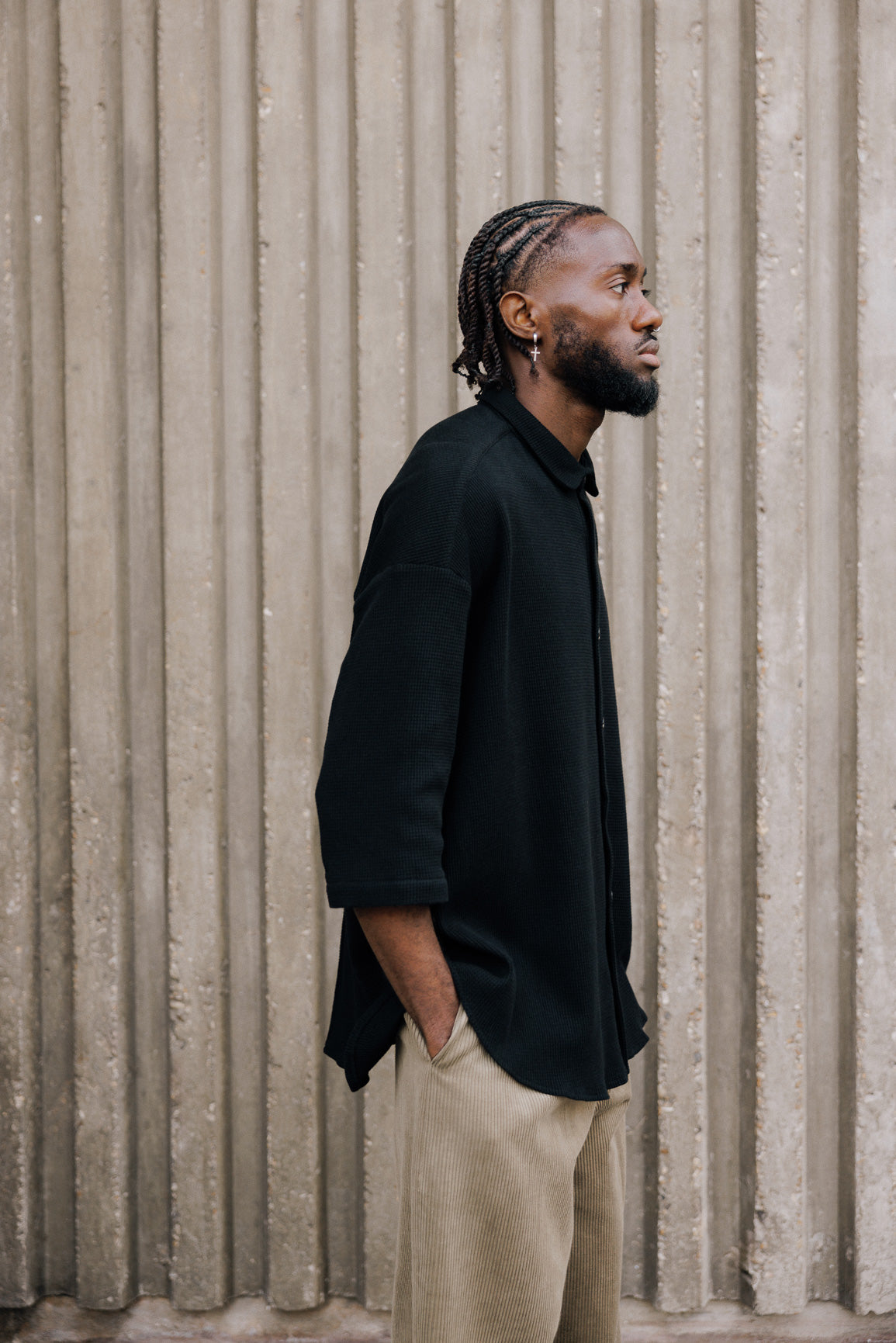 Chemise oversize à manches courtes et col club de la marque Aïdama, modèle Marui en coton nid d’abeille noir. Portée par un mannequin homme et vue de profil.