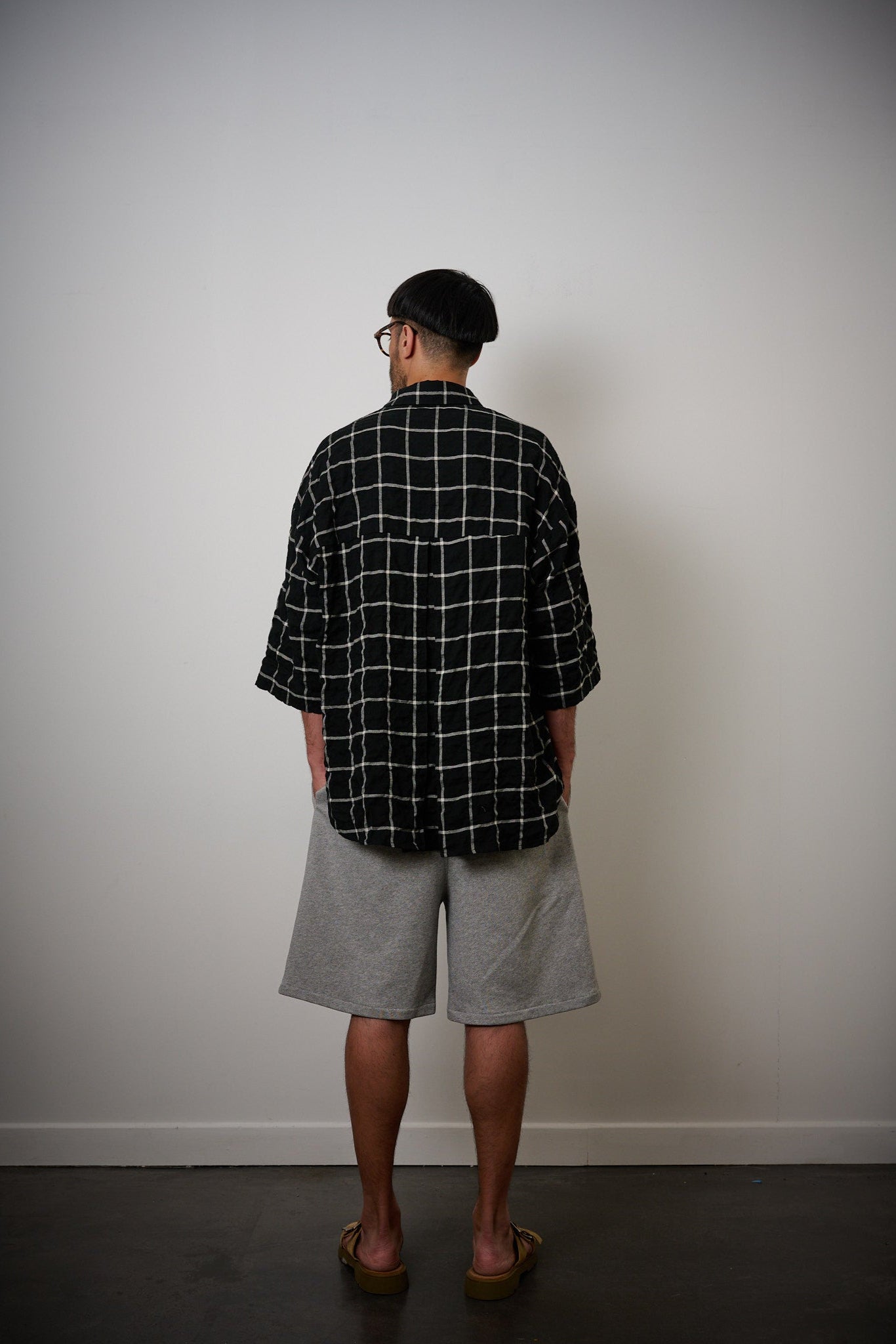 Chemise oversize à manches courtes et col club de la marque Aïdama, modèle Marui en coton seersucker à motif tartan & chevrons noir et blanc. Portée par un mannequin homme et vue de dos.