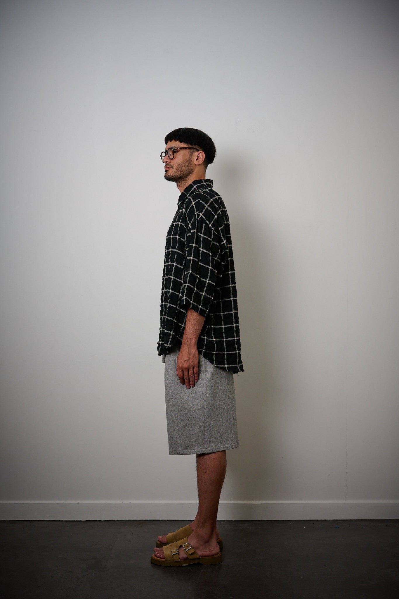 Chemise oversize à manches courtes et col club de la marque Aïdama, modèle Marui en coton seersucker à motif tartan & chevrons noir et blanc. Portée par un mannequin homme et vue de profil.