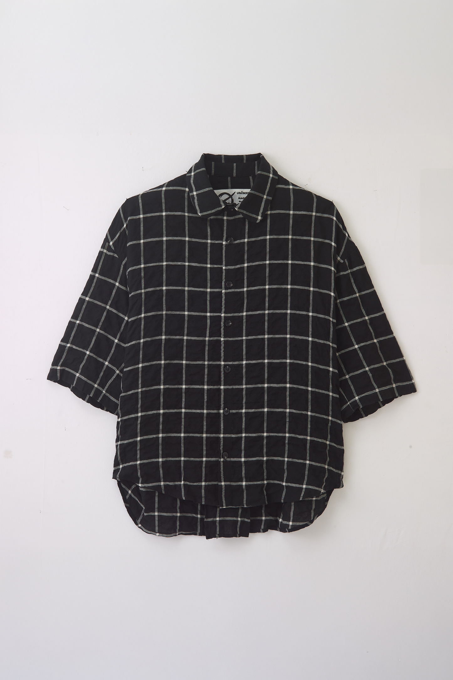 Chemise oversize à manches courtes et col club de la marque Aïdama, modèle Marui en coton seersucker à motif tartan & chevrons noir et blanc. Posée à  plat sur fond blanc.