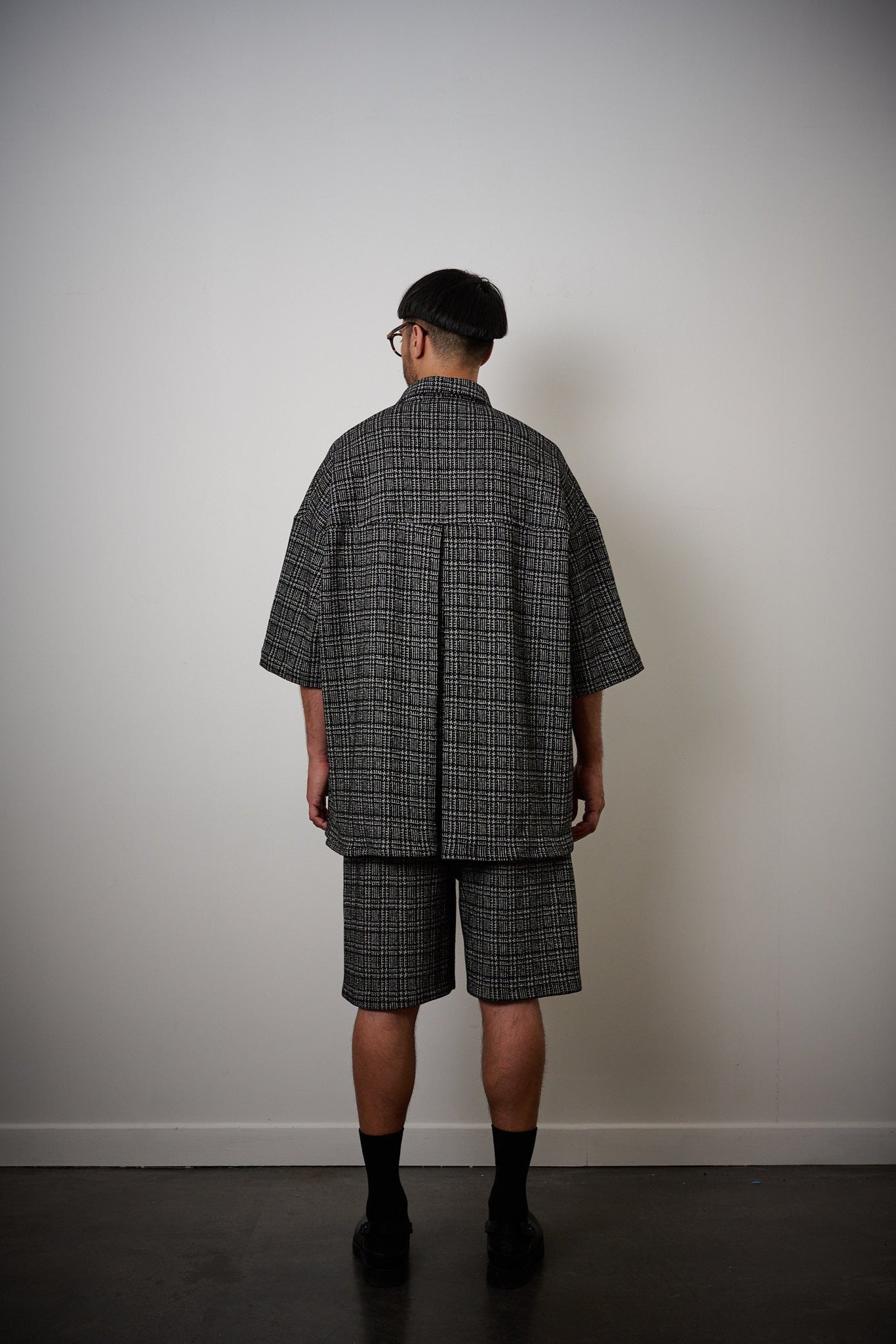 Chemise oversize à manches courtes et col club de la marque Aïdama, modèle Oba en laine à motif géométrique noir et blanc. Portée par un mannequin homme et vue de dos.