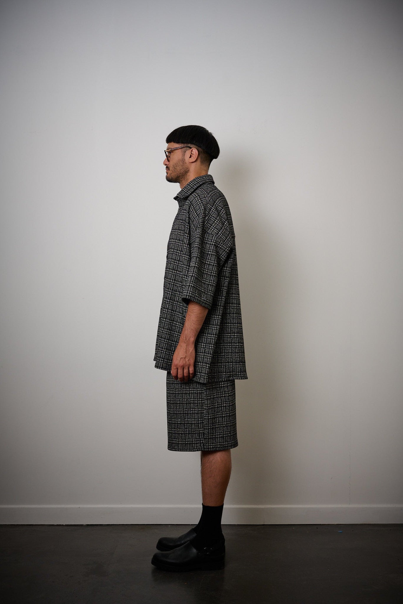 Chemise oversize à manches courtes et col club de la marque Aïdama, modèle Oba en laine à motif géométrique noir et blanc. Portée par un mannequin homme et vue de profil.