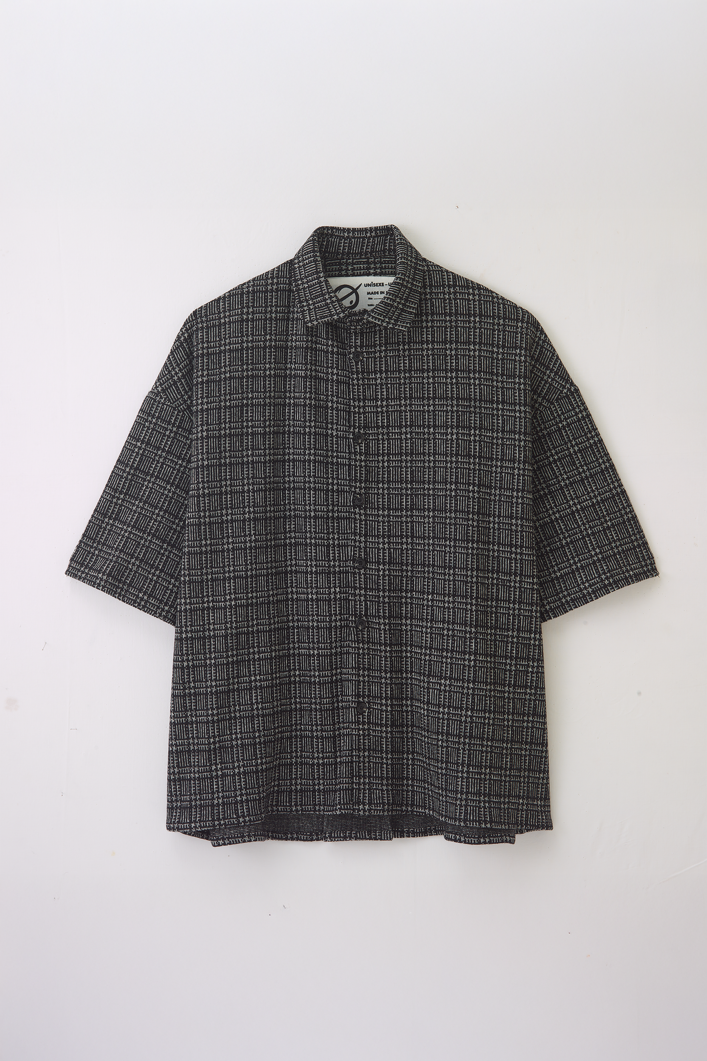 Chemise oversize à manches courtes et col club de la marque Aïdama, modèle Oba en laine à motif géométrique noir et blanc. Posée à plat sur fond blanc.