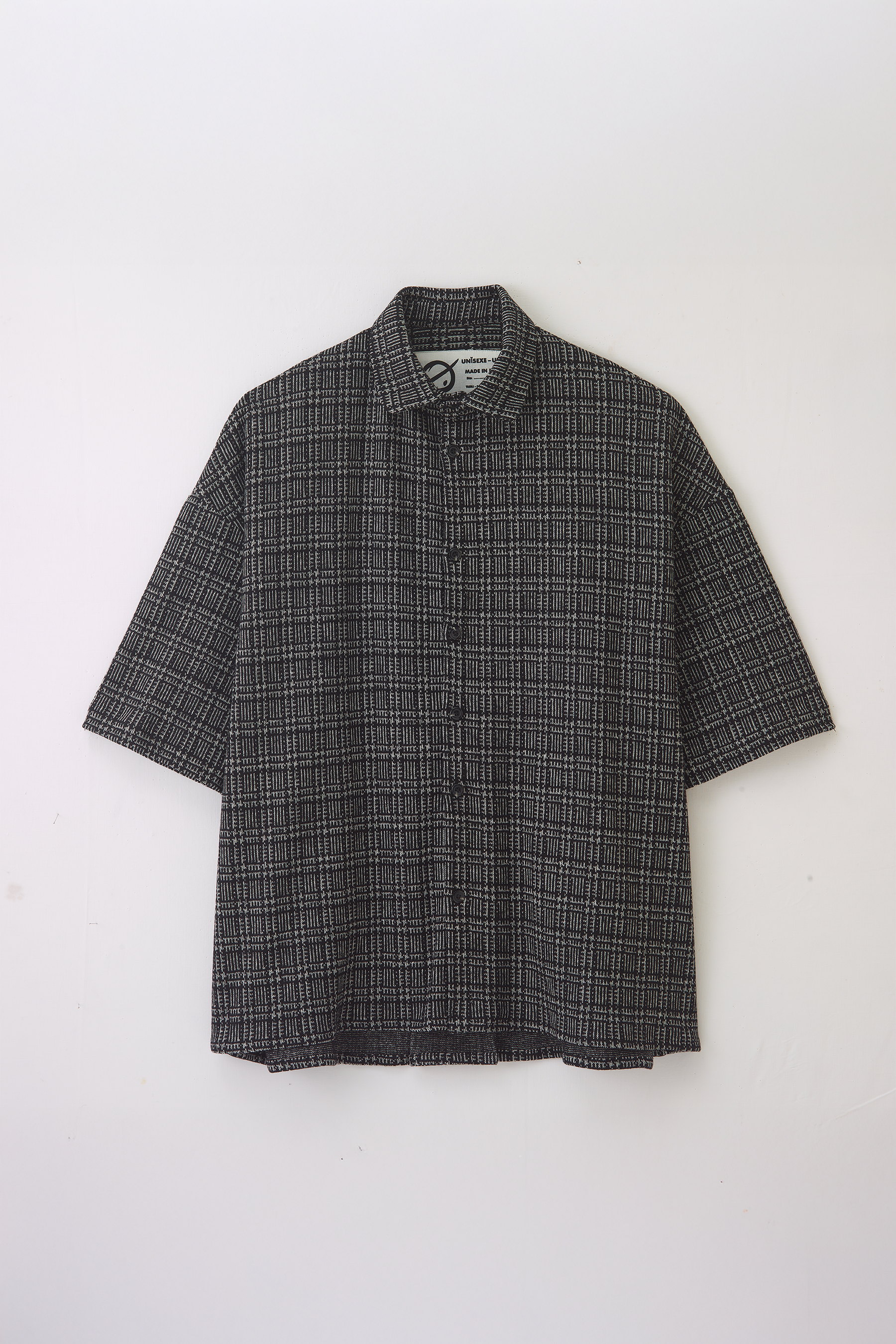 Chemise oversize à manches courtes et col club de la marque Aïdama, modèle Oba en laine à motif géométrique noir et blanc. Posée à plat sur fond blanc.