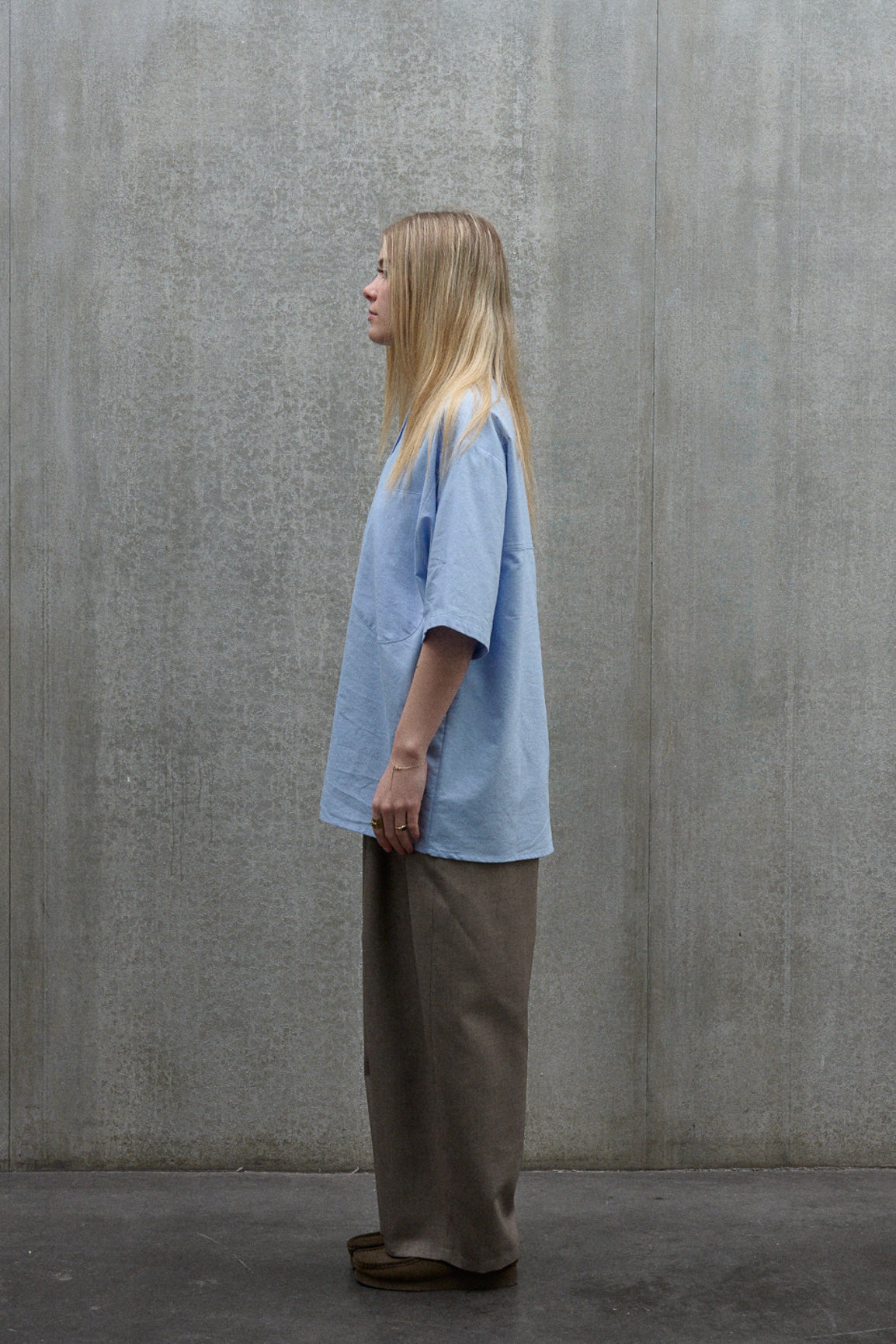 Chemise popover oversize à col tunisien et poche poitrine de la marque Aïdama, en coton piqué bleu. Portée par une mannequin femme et vue de profil.