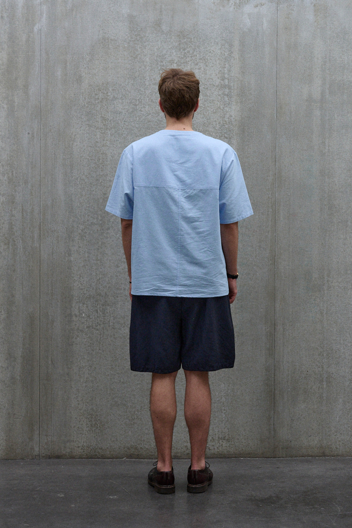 Chemise popover oversize à col tunisien et poche poitrine de la marque Aïdama, en coton piqué bleu. Portée par un mannequin homme et vue de dos.