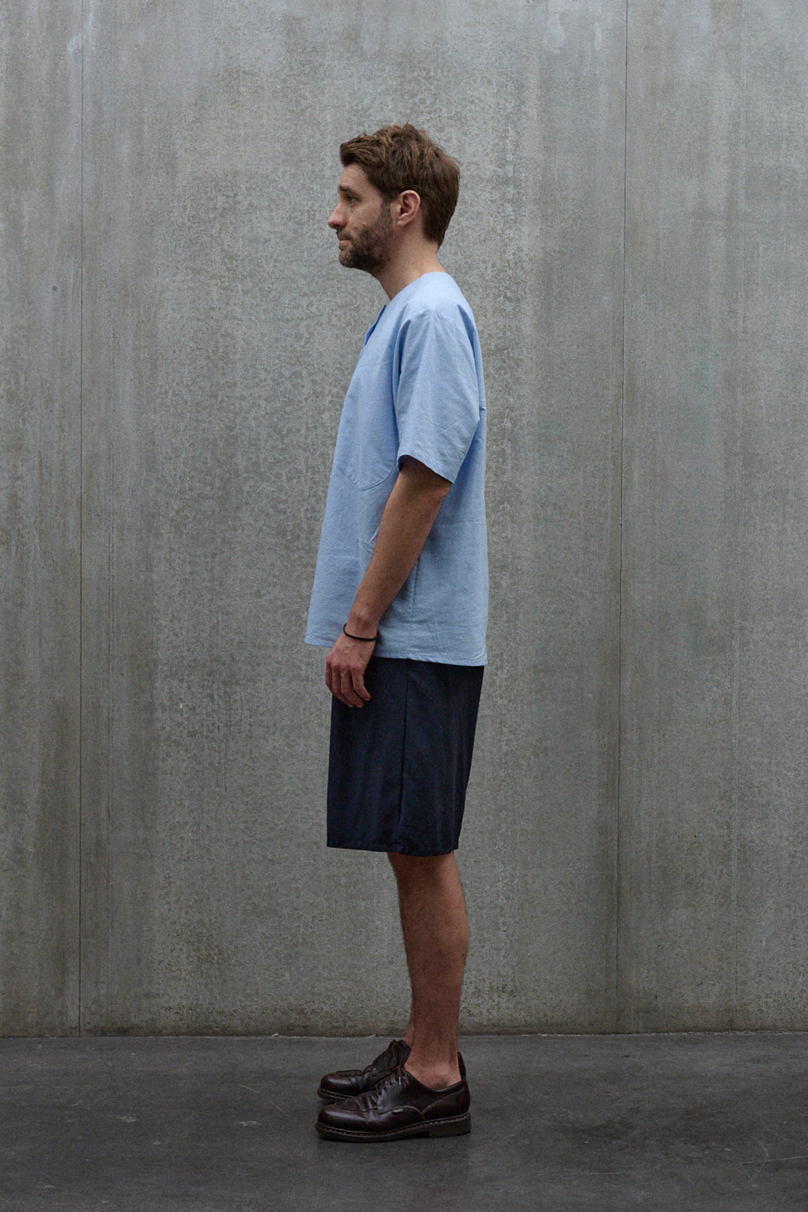Chemise popover oversize à col tunisien et poche poitrine de la marque Aïdama, en coton piqué bleu. Portée par un mannequin homme et vue de profil.