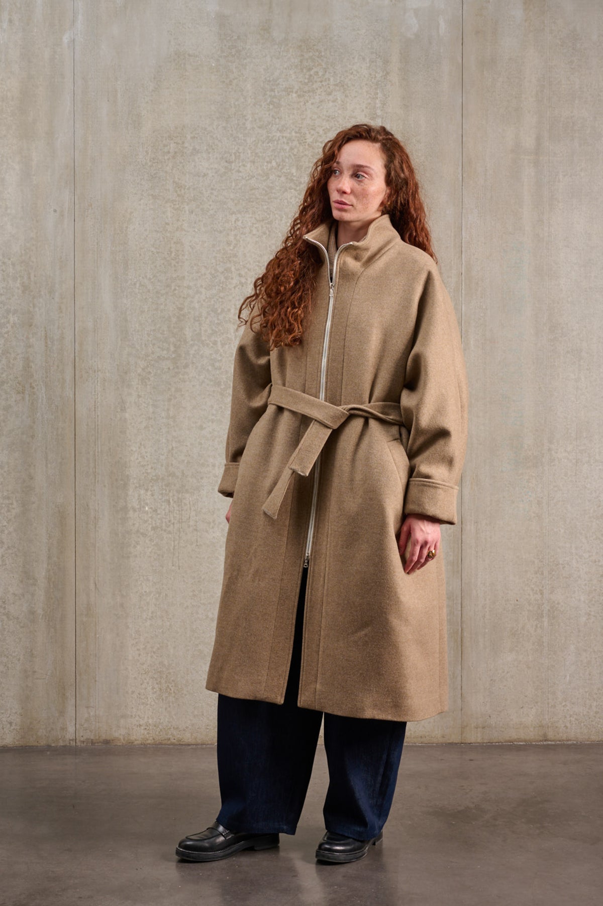 Manteau oversize à manches dolmans de la marque Aïdama, modèle Tanzen en laine et cachemire beige. Porté fermé et ceinturé par une mannequin femme et vu de trois quarts.