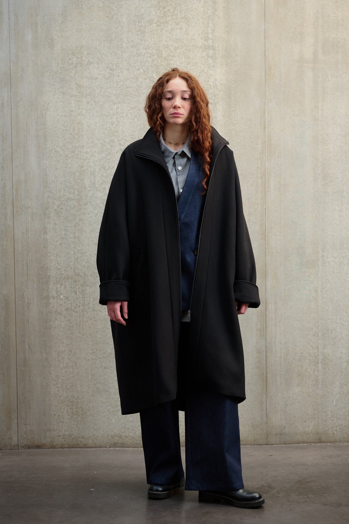 Manteau oversize à manches dolmans de la marque Aïdama, modèle Tanzen en laine feutrée noir. Porté ouvert par une mannequin femme et vu de face.