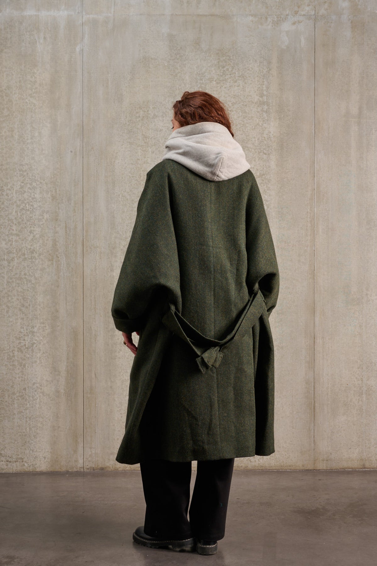 Manteau oversize à manches dolmans de la marque Aïdama, modèle Tanzen en laine, vert à motif chevrons. Porté ouvert et ceinturé par une mannequin femme et vu de dos.