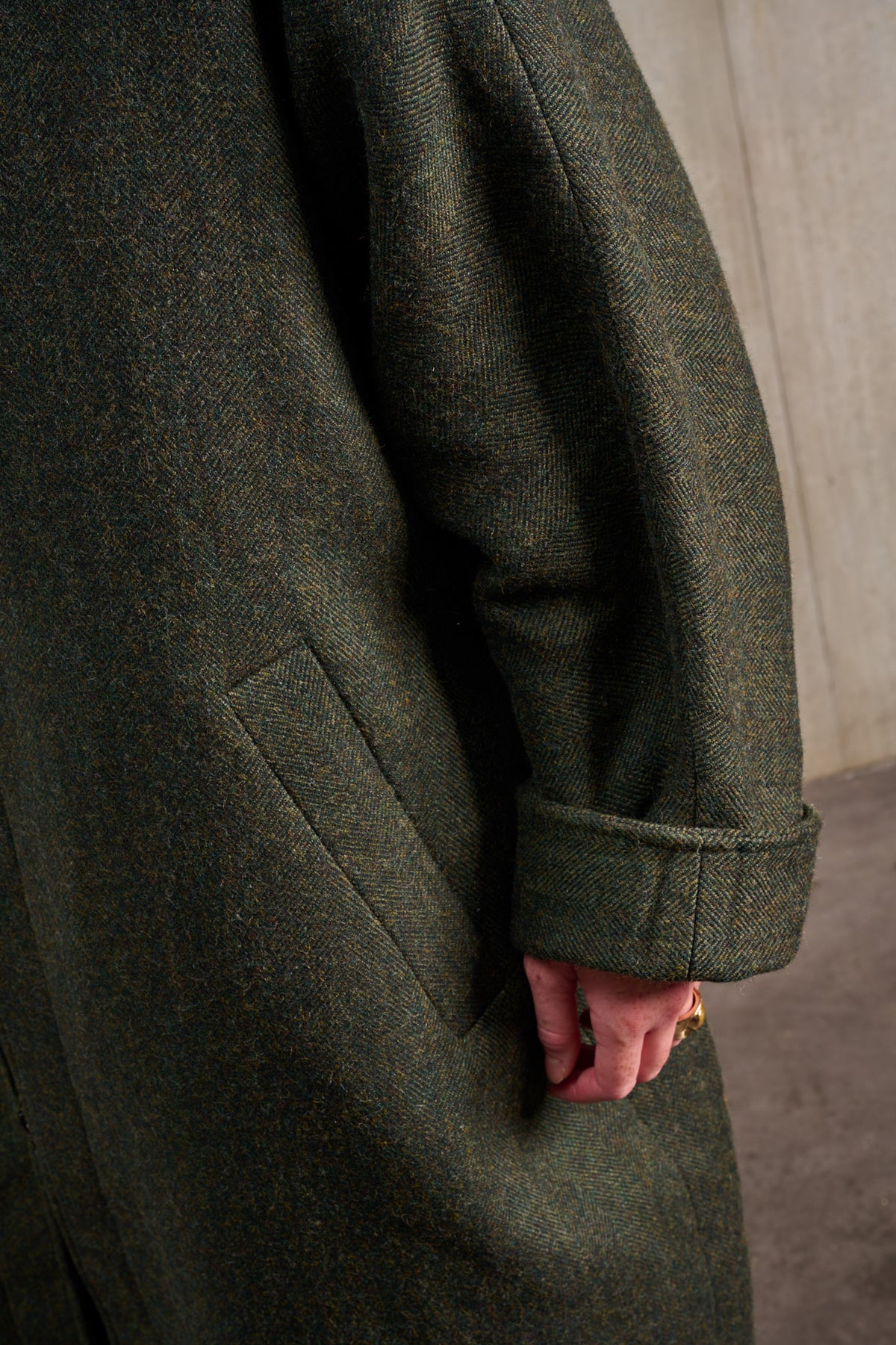 Manteau oversize à manches dolmans de la marque Aïdama, modèle Tanzen en laine, vert à motif chevrons. Porté ouvert par une mannequin femme et vu zoomé sur la manche.