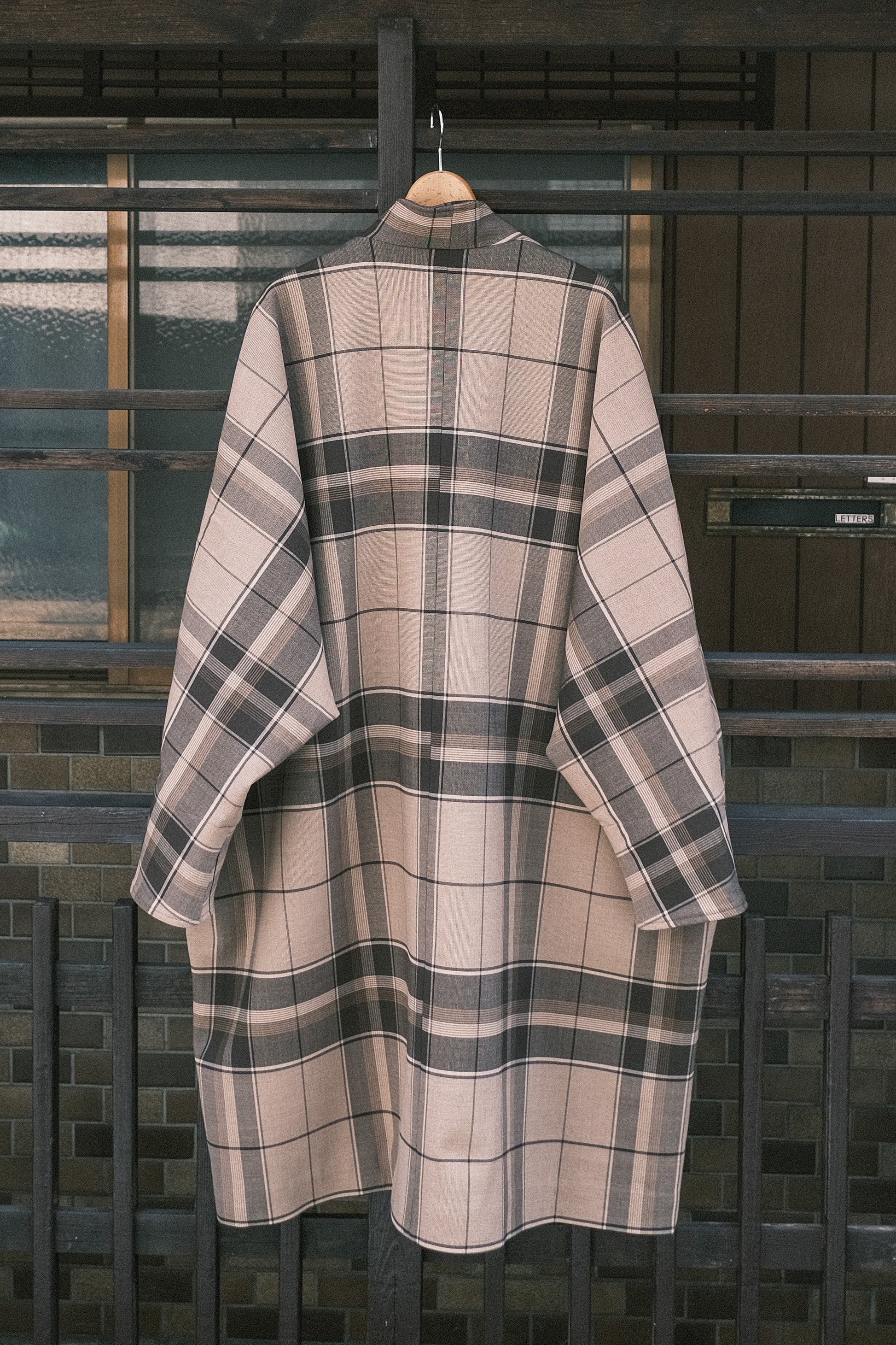 Manteau long à manches dolmans de la marque Aïdama, modèle Tanzen en laine beige à carreaux. Vu de dos sur cintre.