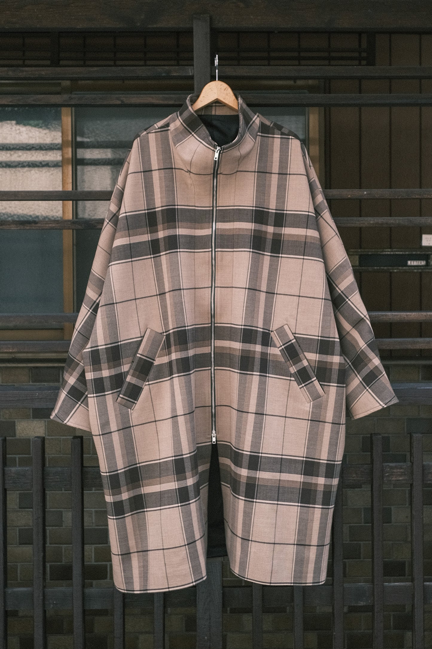 Manteau long à manches dolmans de la marque Aïdama, modèle Tanzen en laine beige à carreaux. Vu de face sur ceintre.