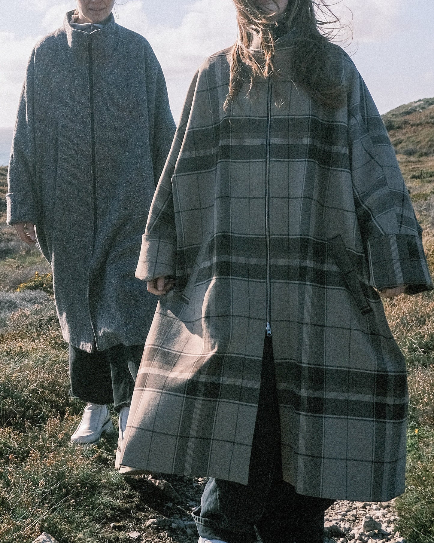 Manteau long à manches dolmans de la marque Aïdama, modèle Tanzen en laine beige à carreaux. Porté par une mannequin femme et vu de face en extérieur. 