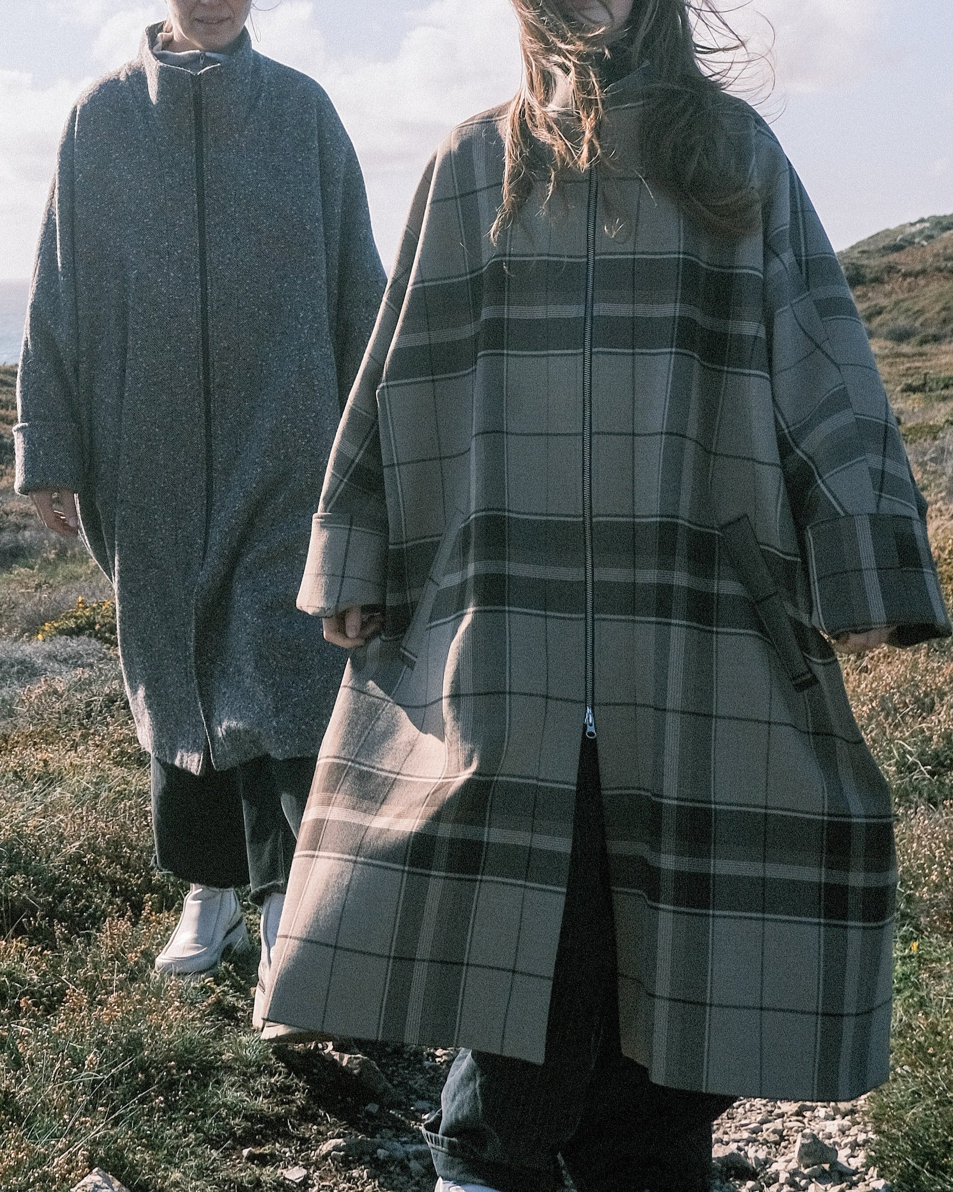 Manteau long à manches dolmans de la marque Aïdama, modèle Tanzen en laine beige à carreaux. Porté par une mannequin femme et vu de face en extérieur. 