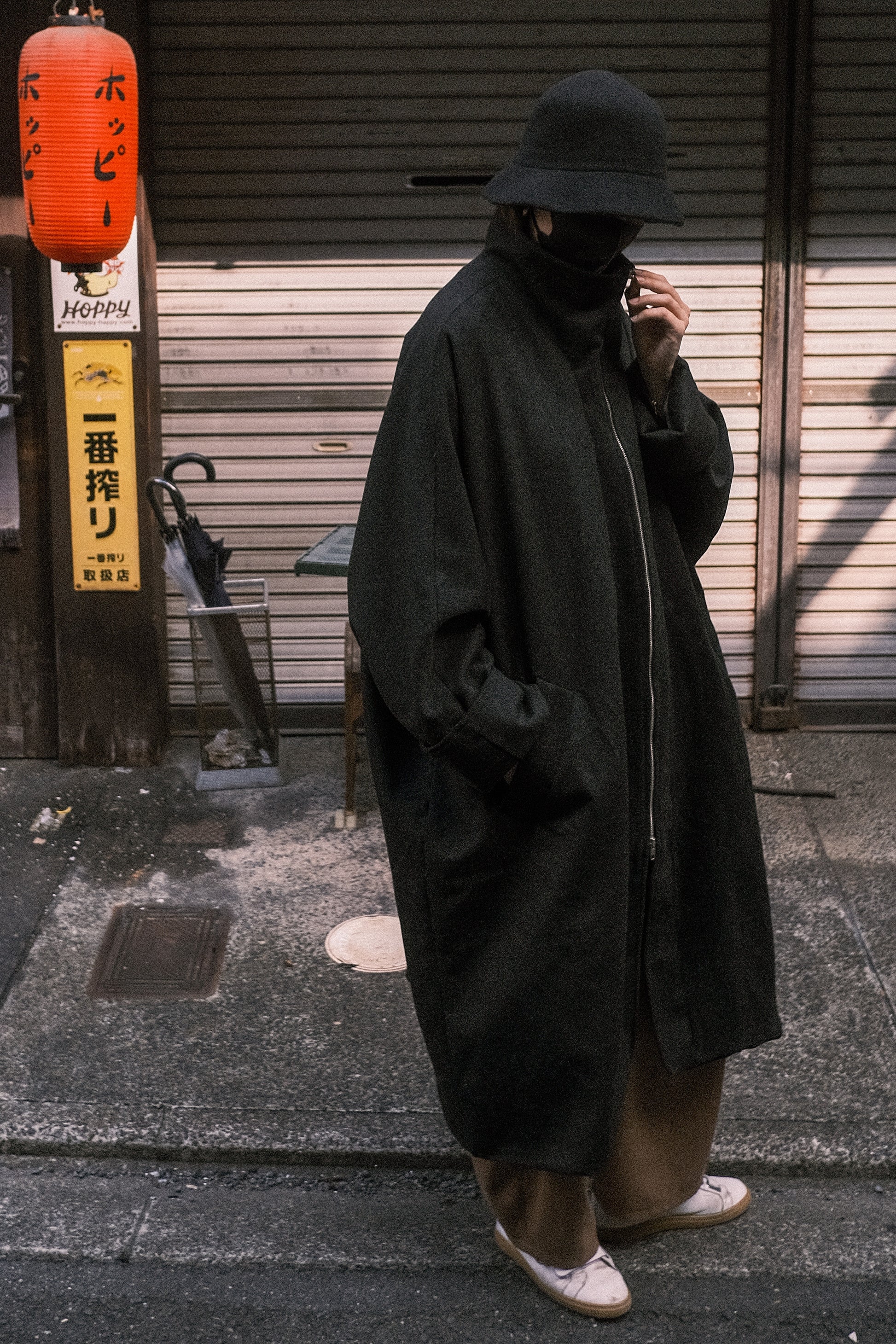 Manteau long à manches dolmans de la marque Aïdama, modèle Tanzen en laine noire. Porté par un mannequin homme et vu de face en extérieur au Japon.