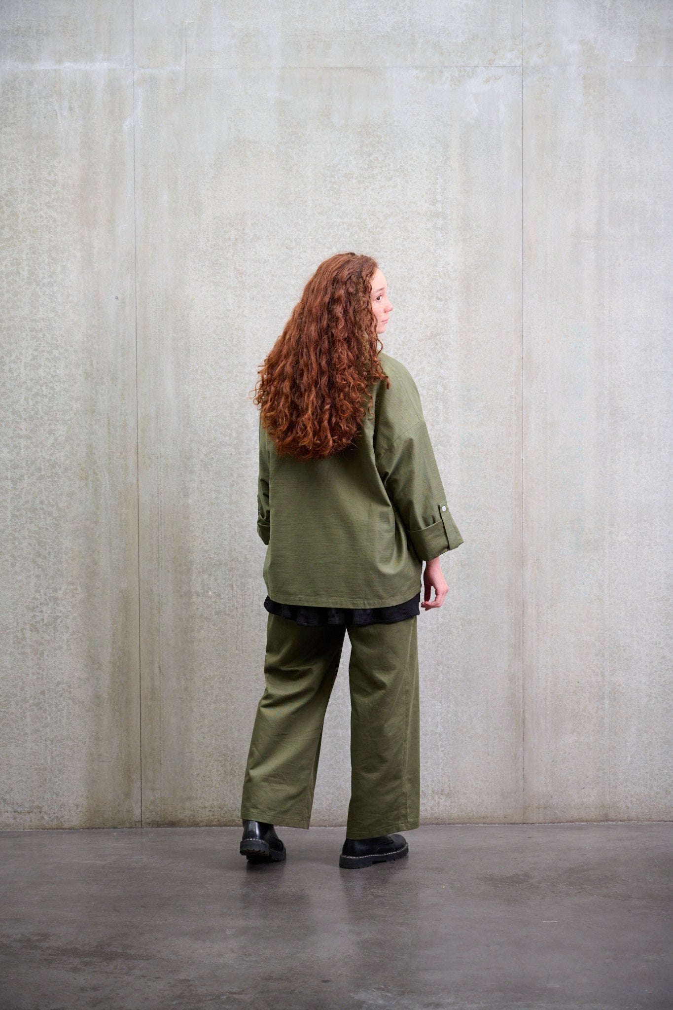 Pantalon droit à coupe ample en coton vert avec sangles de réglages de la marque Aïdama. Porté par une mannequin femme et vu de dos.