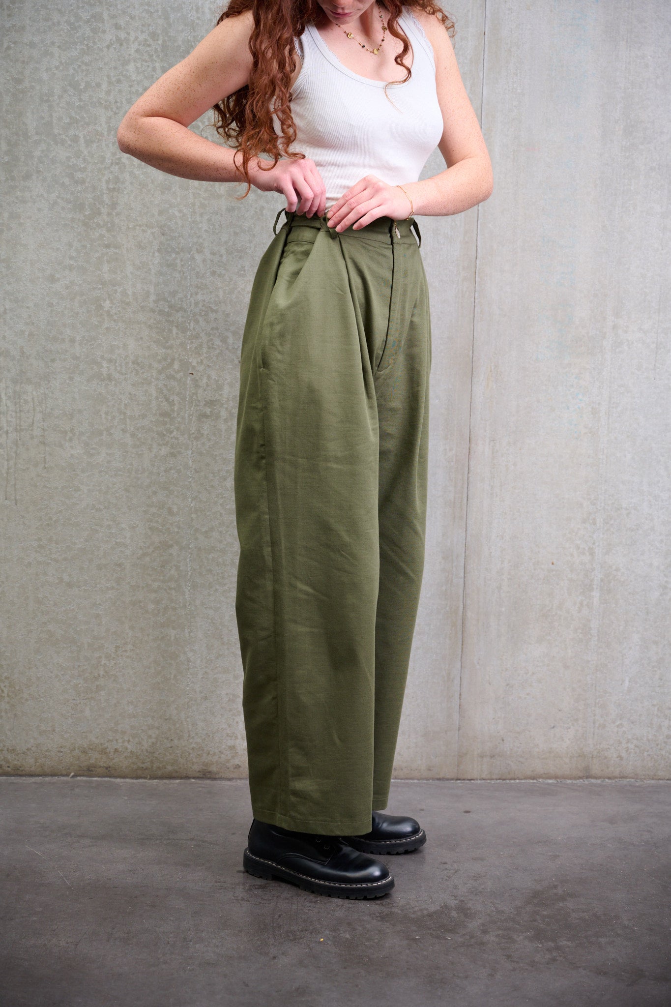 Pantalon droit à coupe ample en coton vert avec sangles de réglages de la marque Aïdama. Porté par une mannequin femme et vue de profil zoomée sur le détail du réglage dela taille.