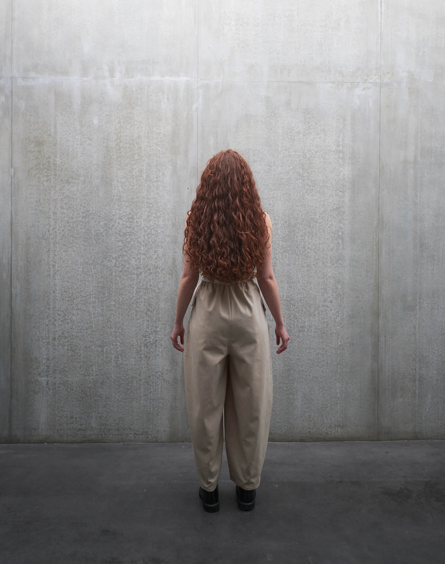 Pantalon circulaire Aïdama, coupe ballon en coton beige. Porté par une mannequin femme et vu de dos.