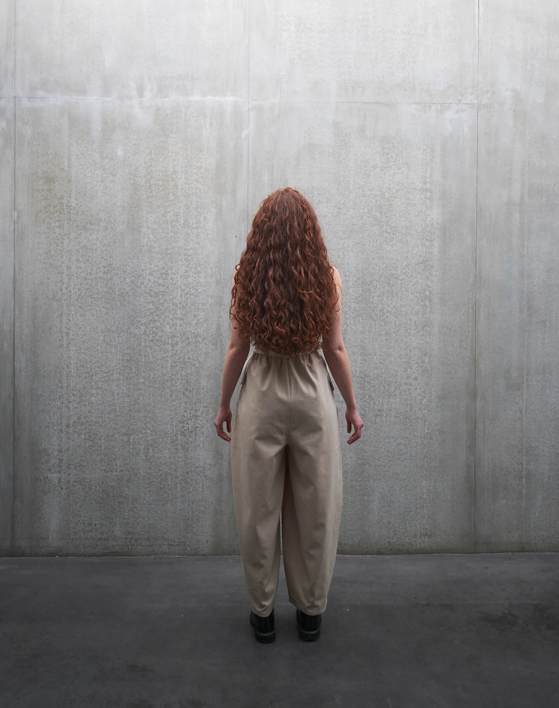 Pantalon circulaire Aïdama, coupe ballon en coton beige. Porté par une mannequin femme et vu de dos.