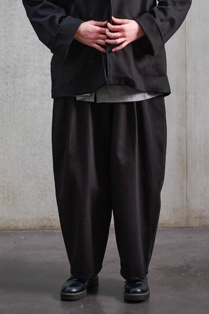 Pantalon circulaire unisexe de la marque Aïdama, coupe ballon en sergé de coton noir. Porté par une mannequin femme et vu zoomé sur les jambes.