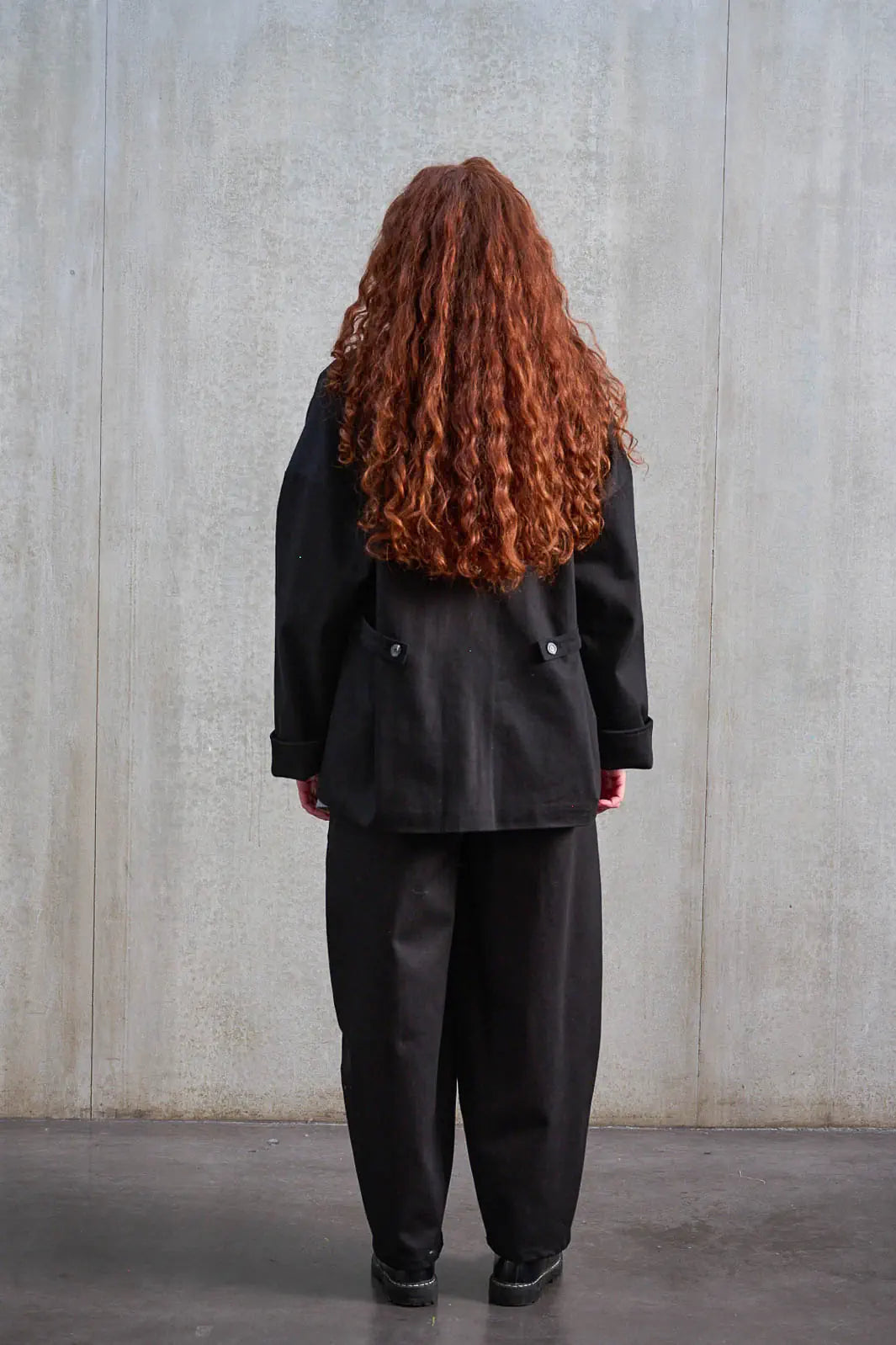 Pantalon circulaire unisexe de la marque Aïdama, coupe ballon en sergé de coton noir. Porté par une mannequin femme et vu de dos.