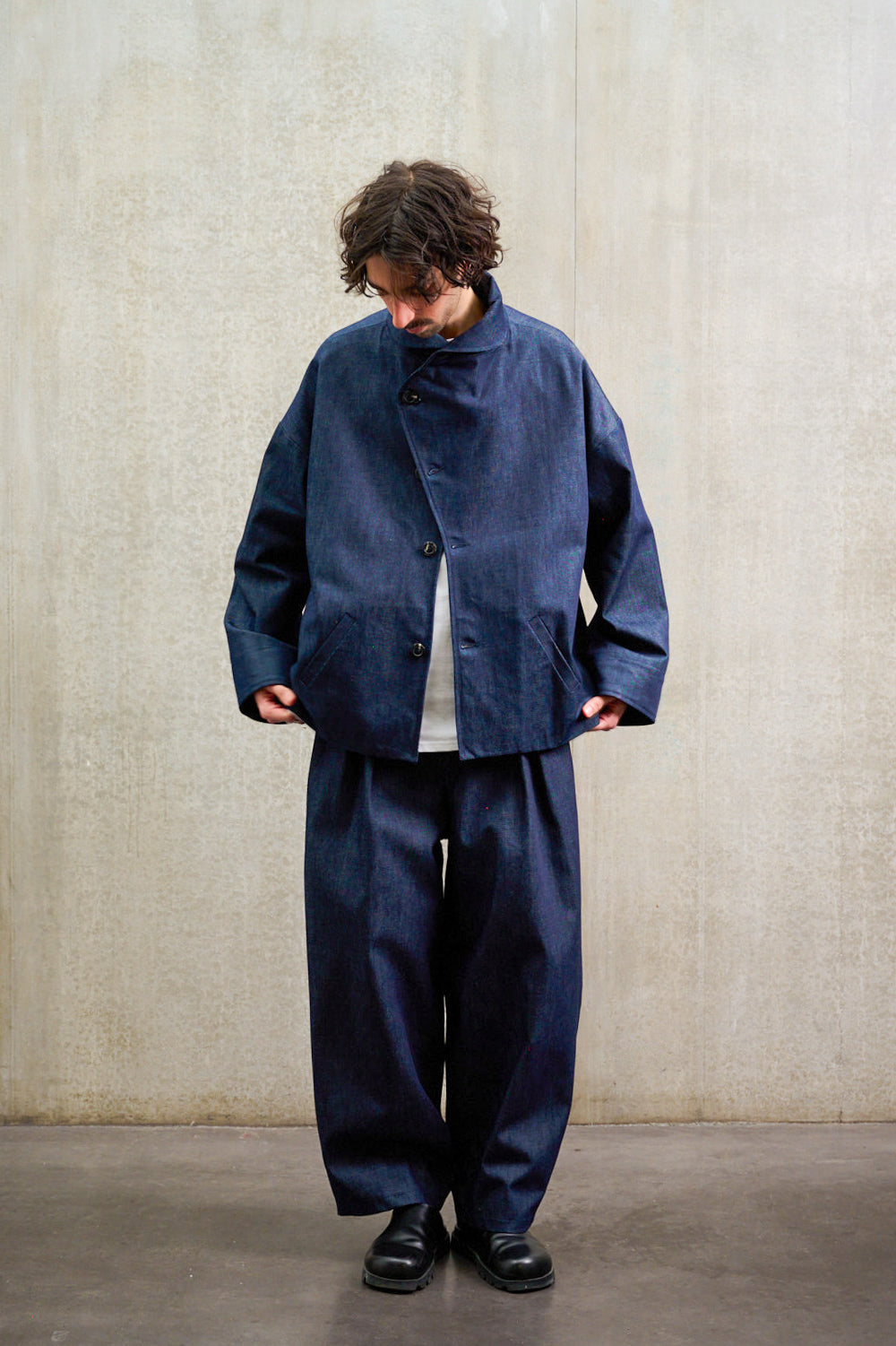 Pantalon circulaire Aïdama, coupe ballon en denim brut. Porté par un mannequin homme et vu de face avec une veste.