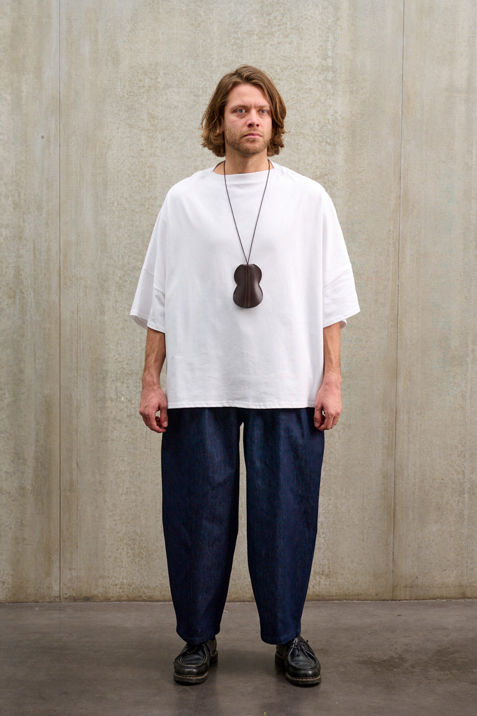 Pantalon circulaire Aïdama coupe ballon en denim brut. Porté par un mannequin homme et vu de face.