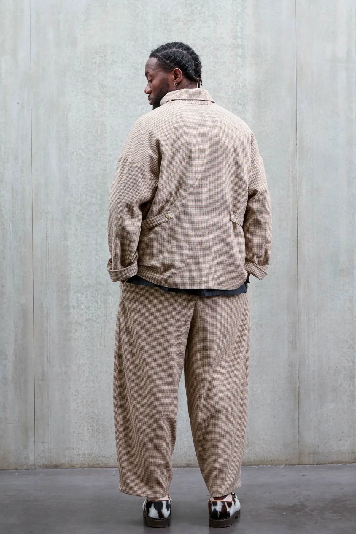 Pantalon circulaire unisexe de la marque Aïdama, coupe ballon en laine marron à motif pied de poule. Porté par une mannequin homme et vu de dos.